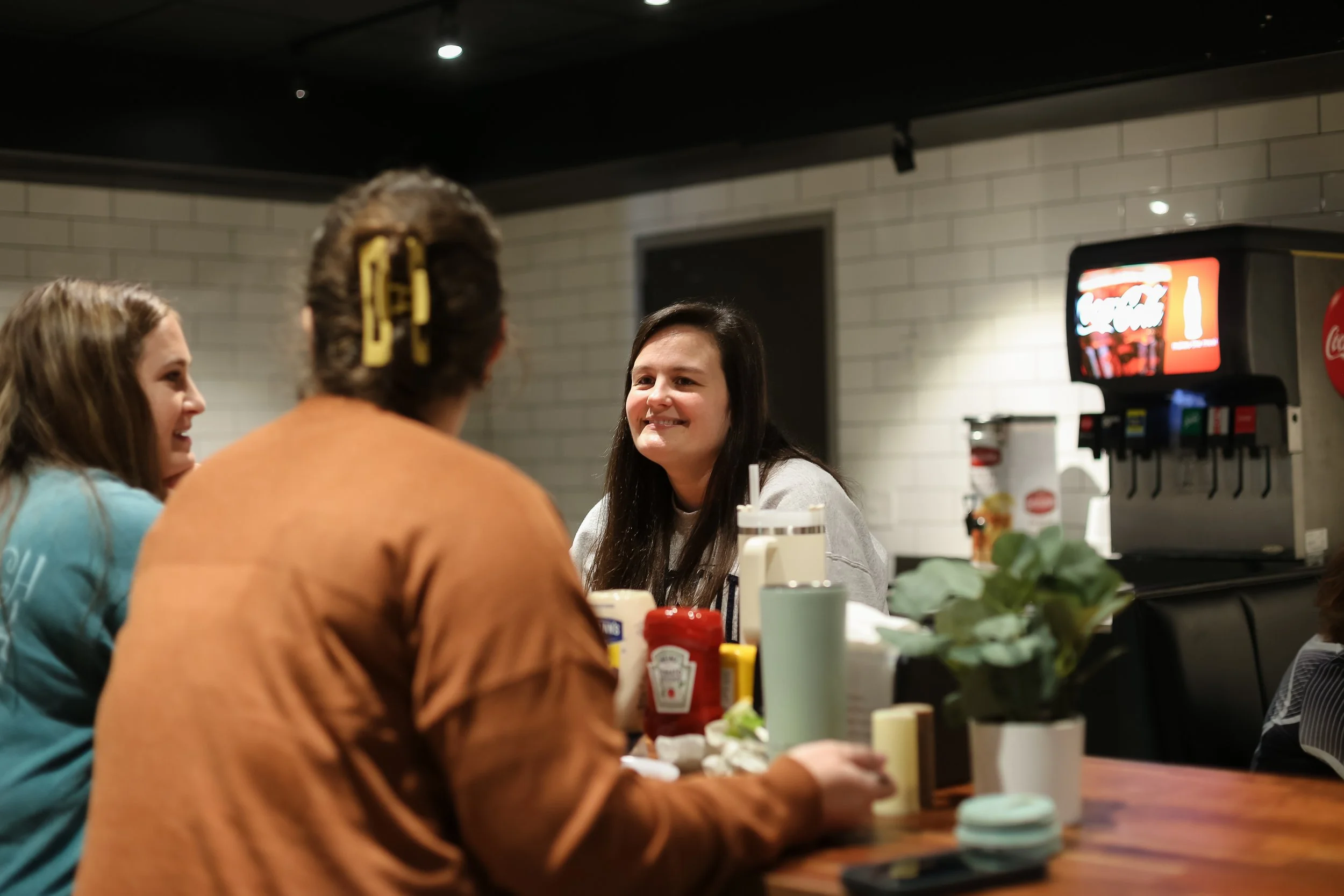 Two retreat attendees are sitting at a table in the cozy dining room at Woodlands Camp. One faces the camera with a warm smile, while the other is seen from behind.