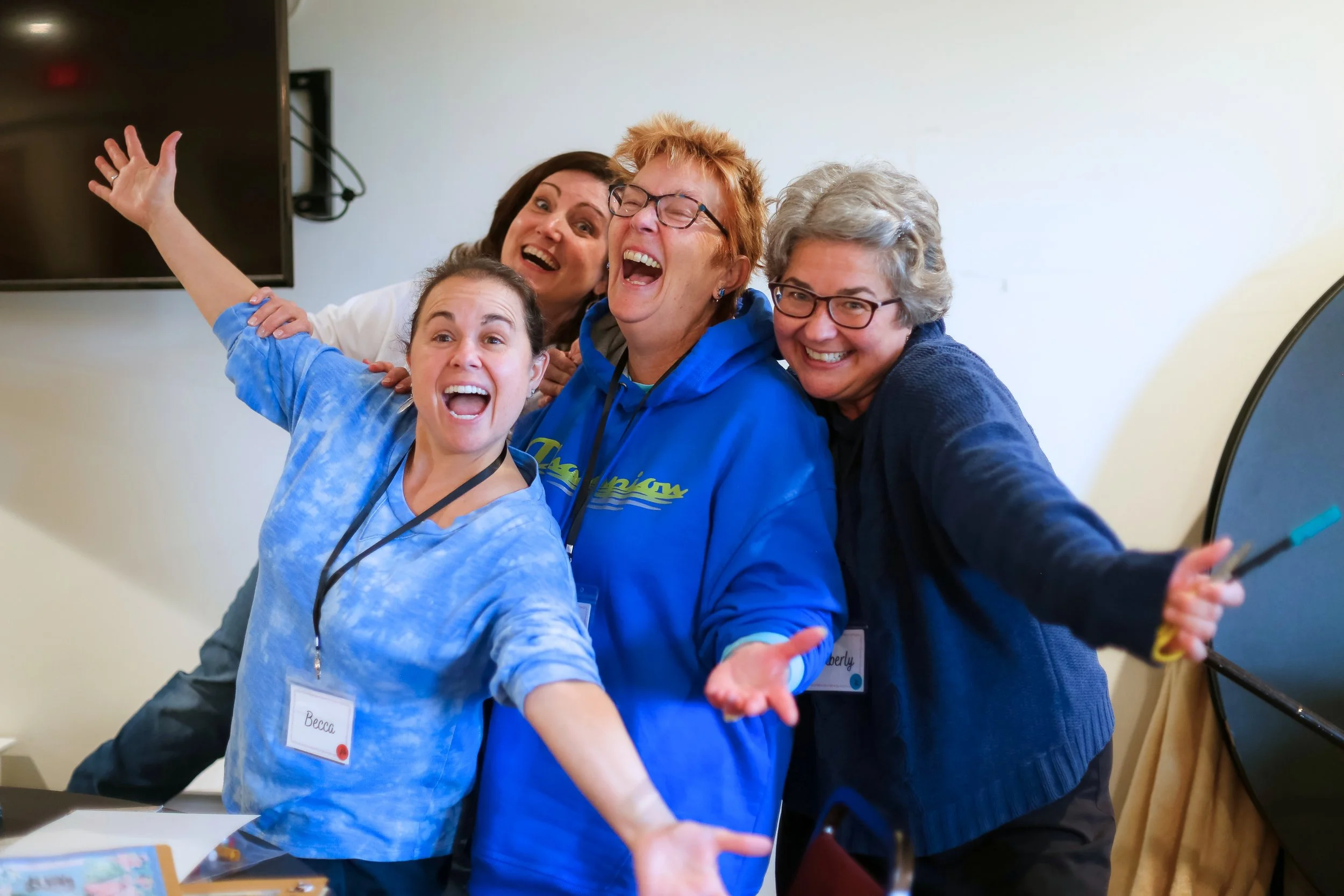 Four women smiling with open arms