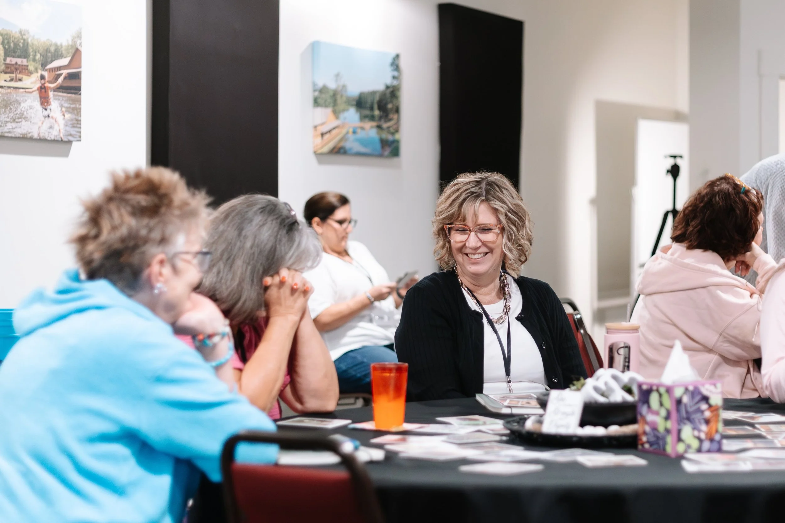Three women sitting around a table during a Large Group session, smiling and talking