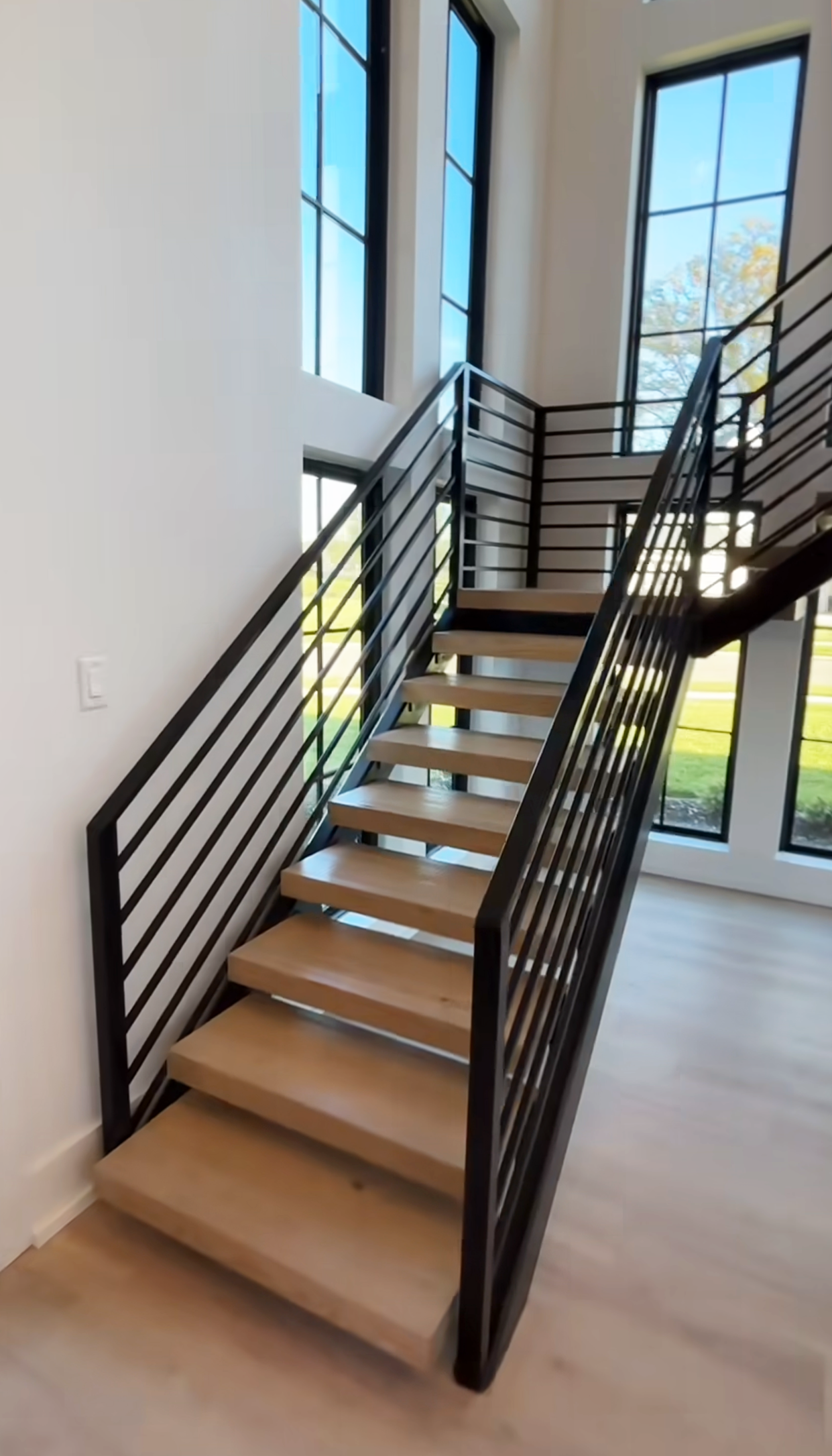 Modern indoor staircase with wooden steps, black metal railings, and large windows letting in natural light.