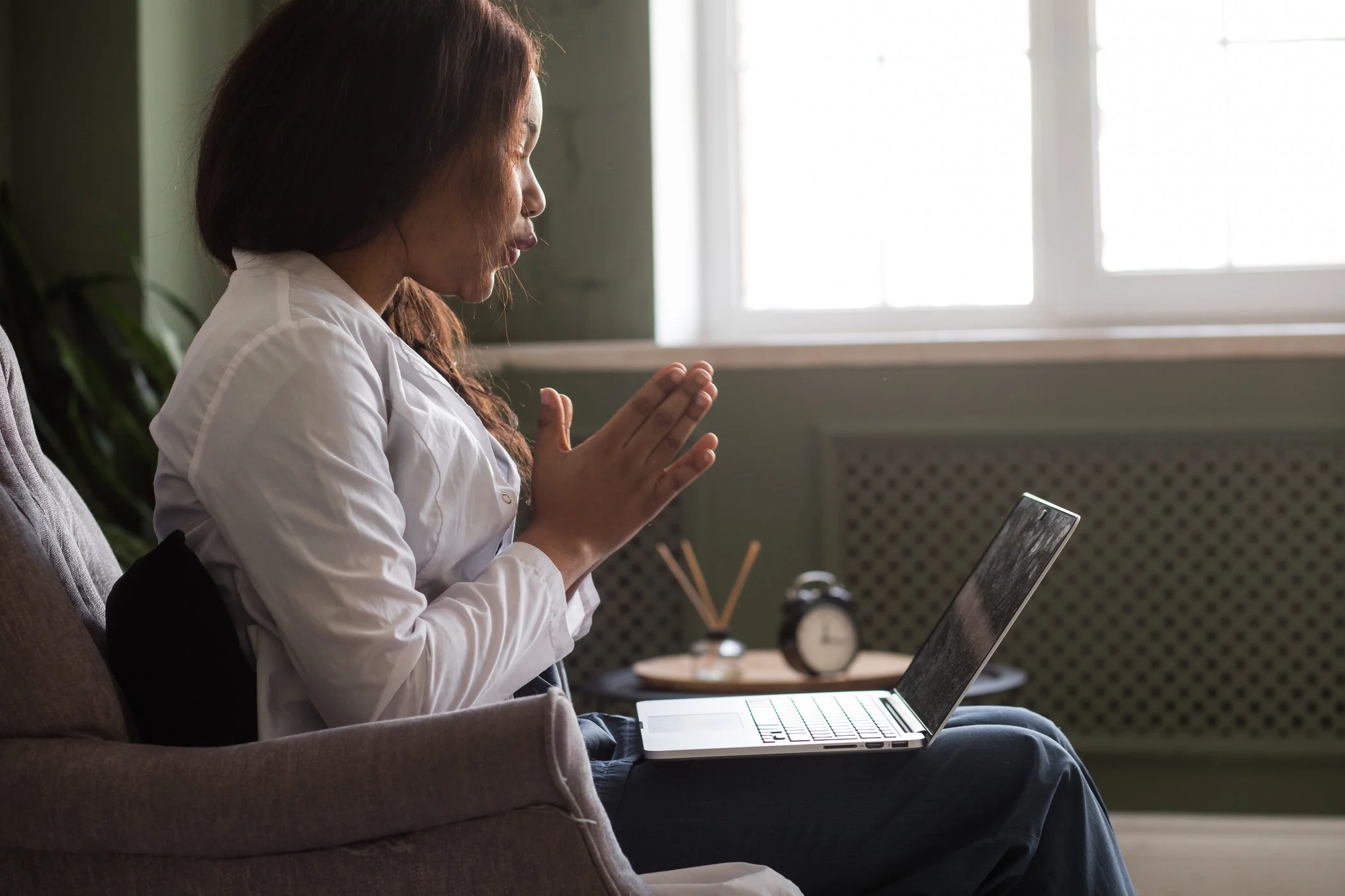 Woman Sitting on a couch with a laptop talking to therapist via telehealth