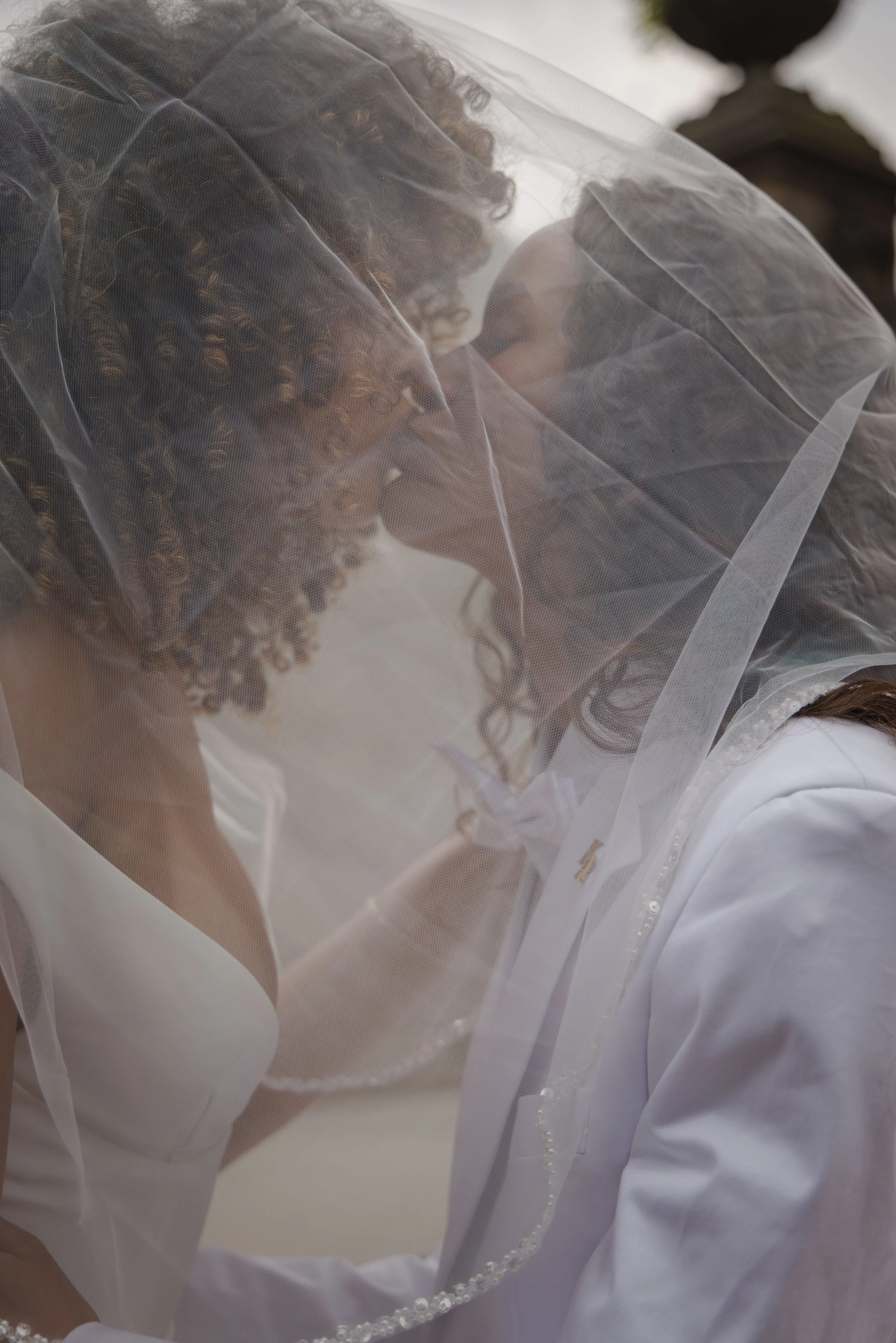 Close-up of a bride wearing a white dress with a sheer veil over her face.
