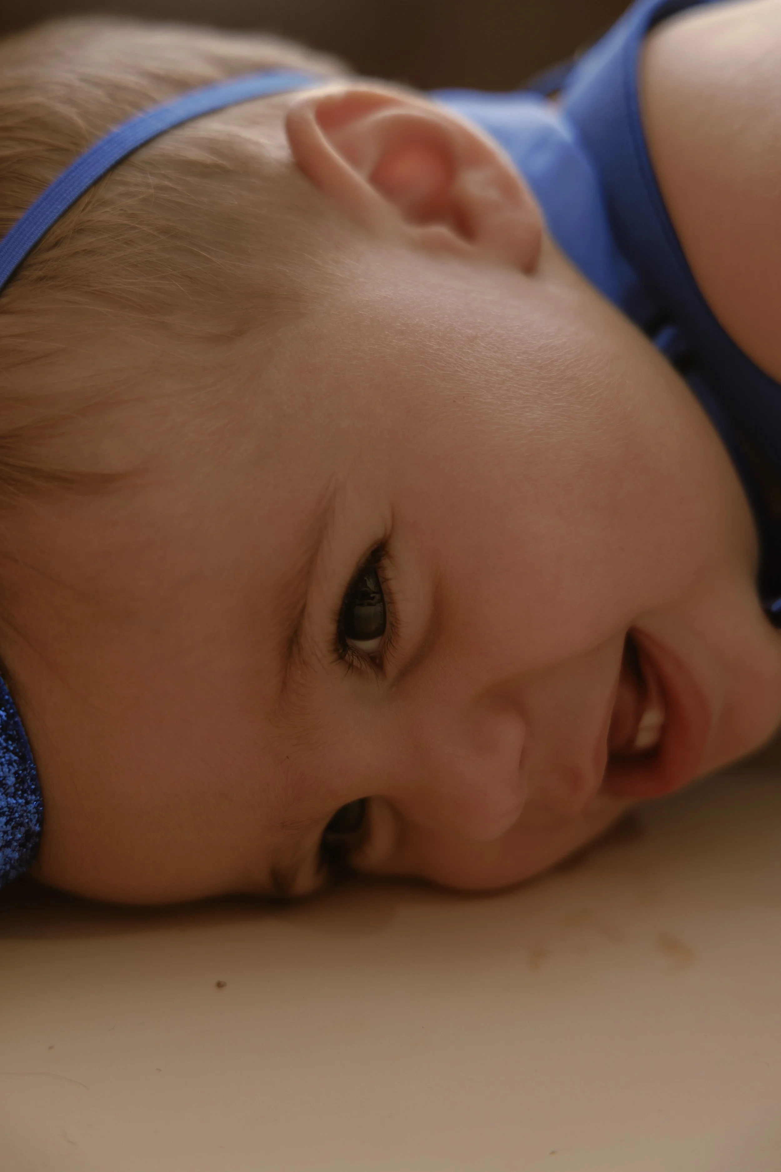 Close-up of a child's face with eyes closed, lying on a flat surface, wearing a blue headband and a blue shirt.