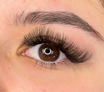 Close-up of a person's eye with long, voluminous eyelashes and well-groomed eyebrows.