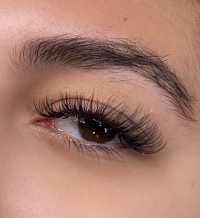 Close-up of a person's eye with brown iris and long, curled eyelashes.