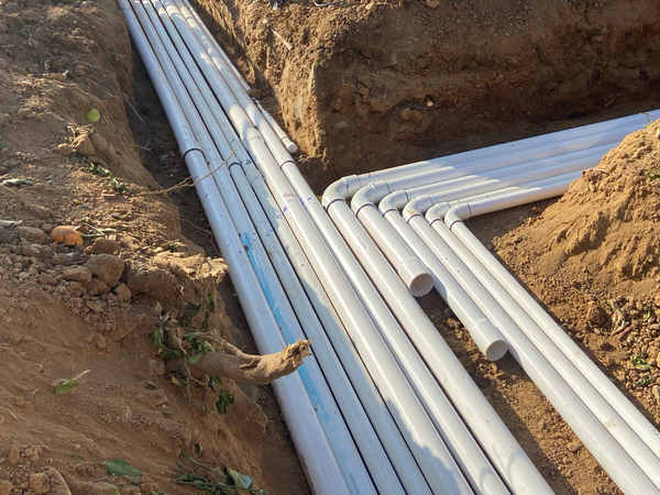 Multiple white PVC pipes are laid in a trench in the ground, likely for plumbing or irrigation.