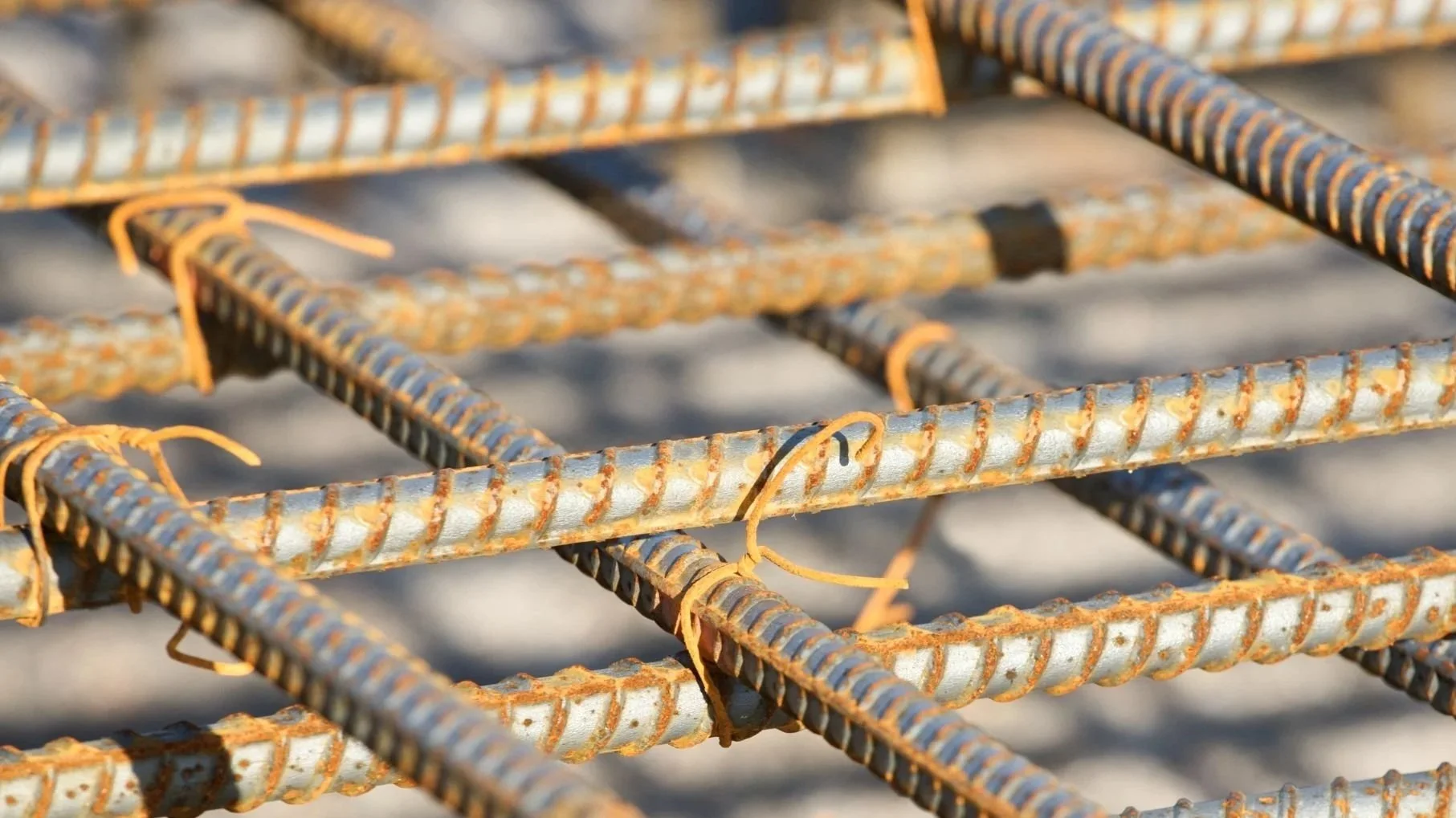 Close-up of rusted steel rebar grid tied with orange plastic ties, used in concrete reinforcement.