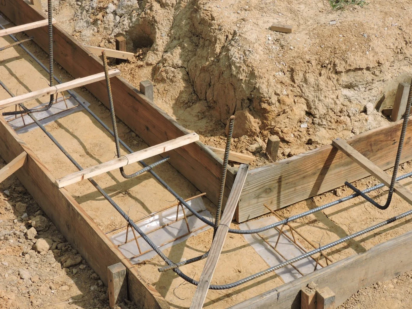 Construction site showing wooden formwork and rebar for concrete foundation.
