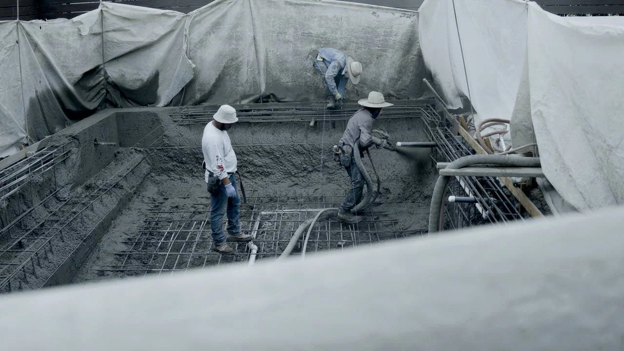 Construction workers pouring and leveling concrete inside a building foundation.