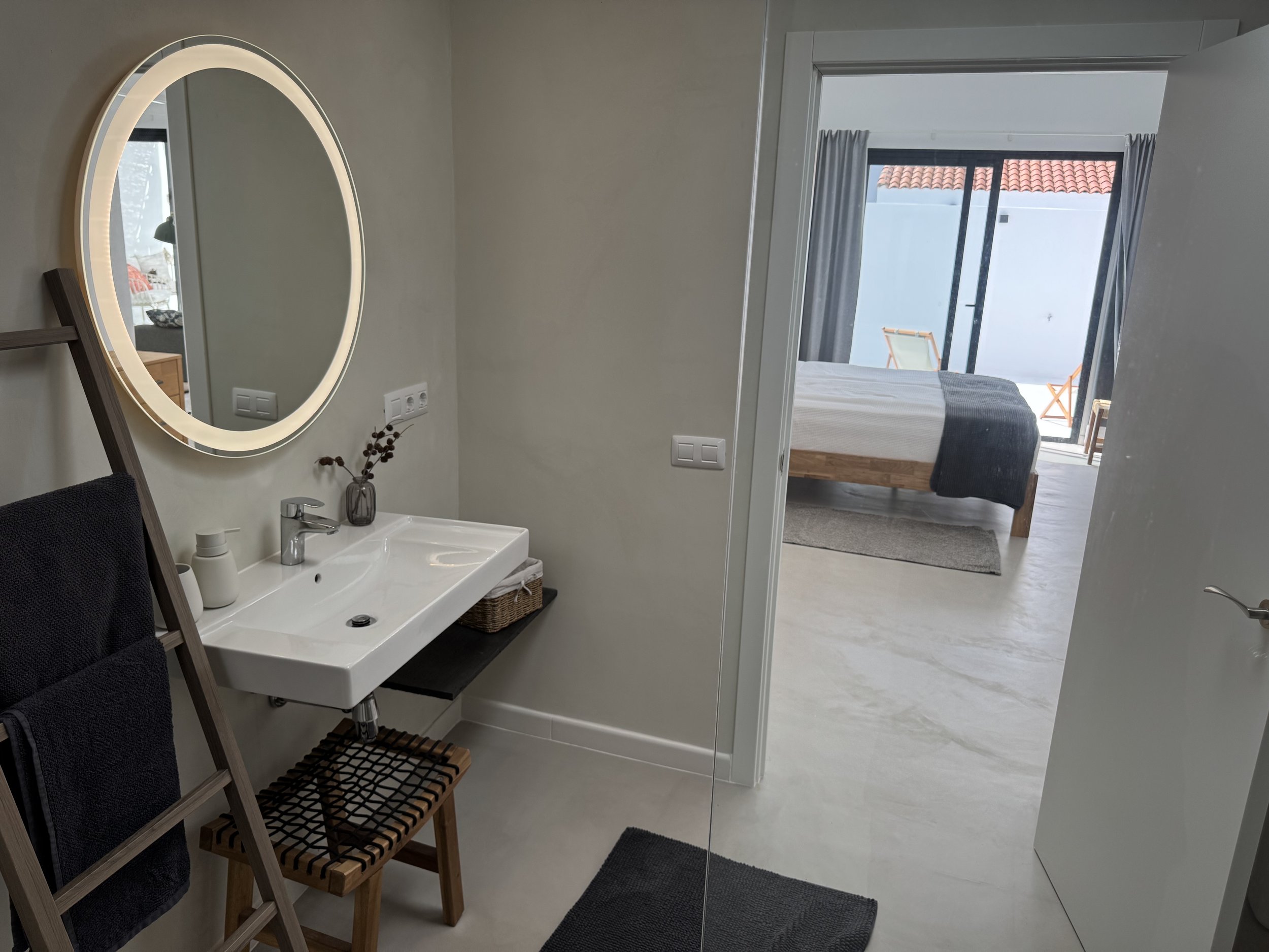 Minimalist bathroom with round mirror and bedroom view at Casita Luna Lanzarote