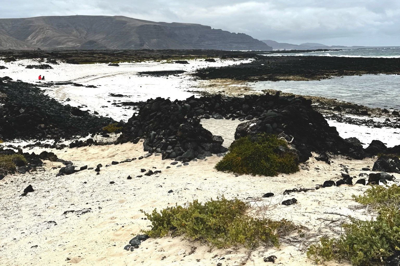 Volcanic coastline with pale sand, black lava and mountains in northern Lanzarote.