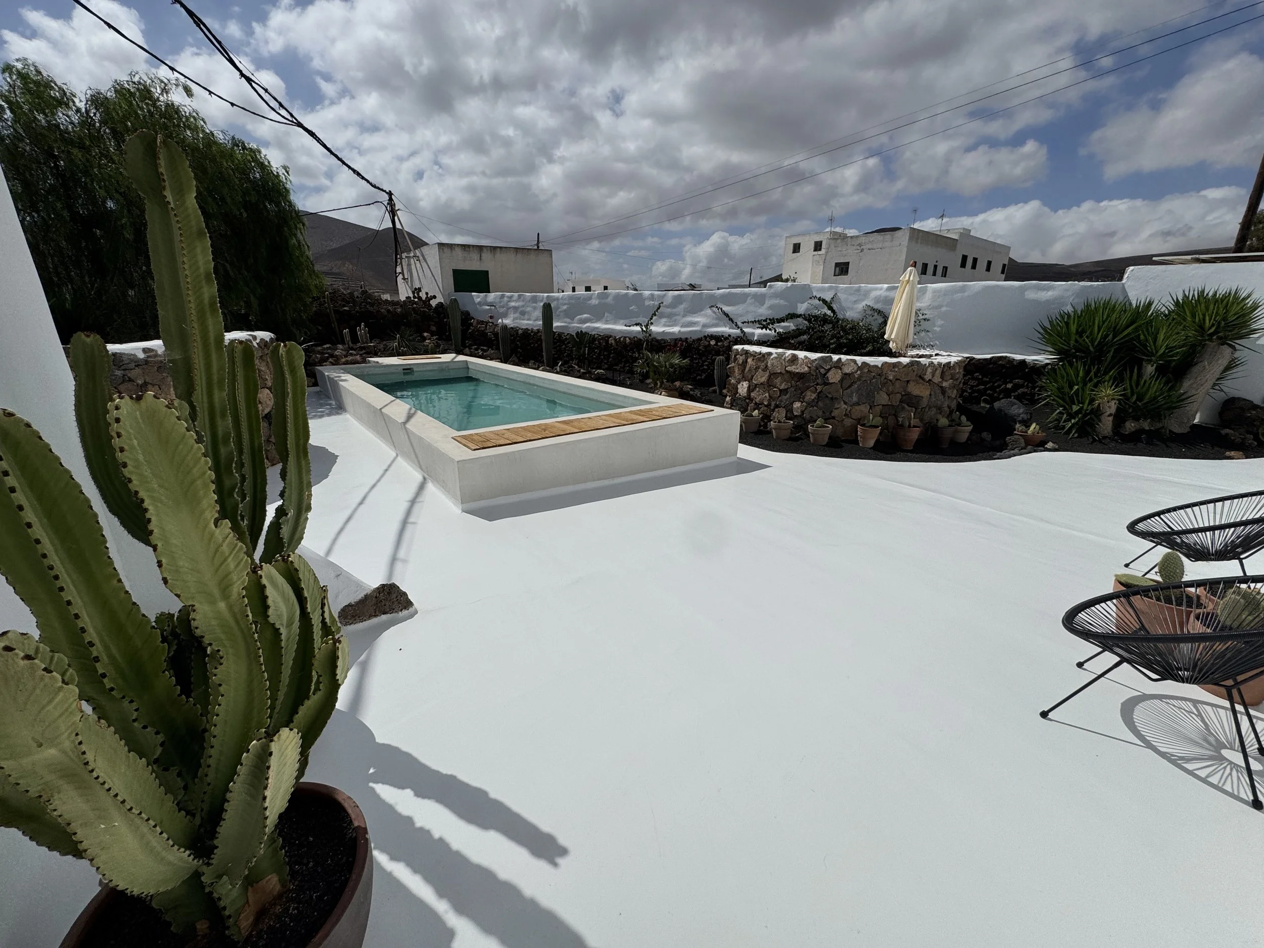 Swimming pool surrounded by tropical trees and volcanic garden at Casitas Santa Rita Lanzarote