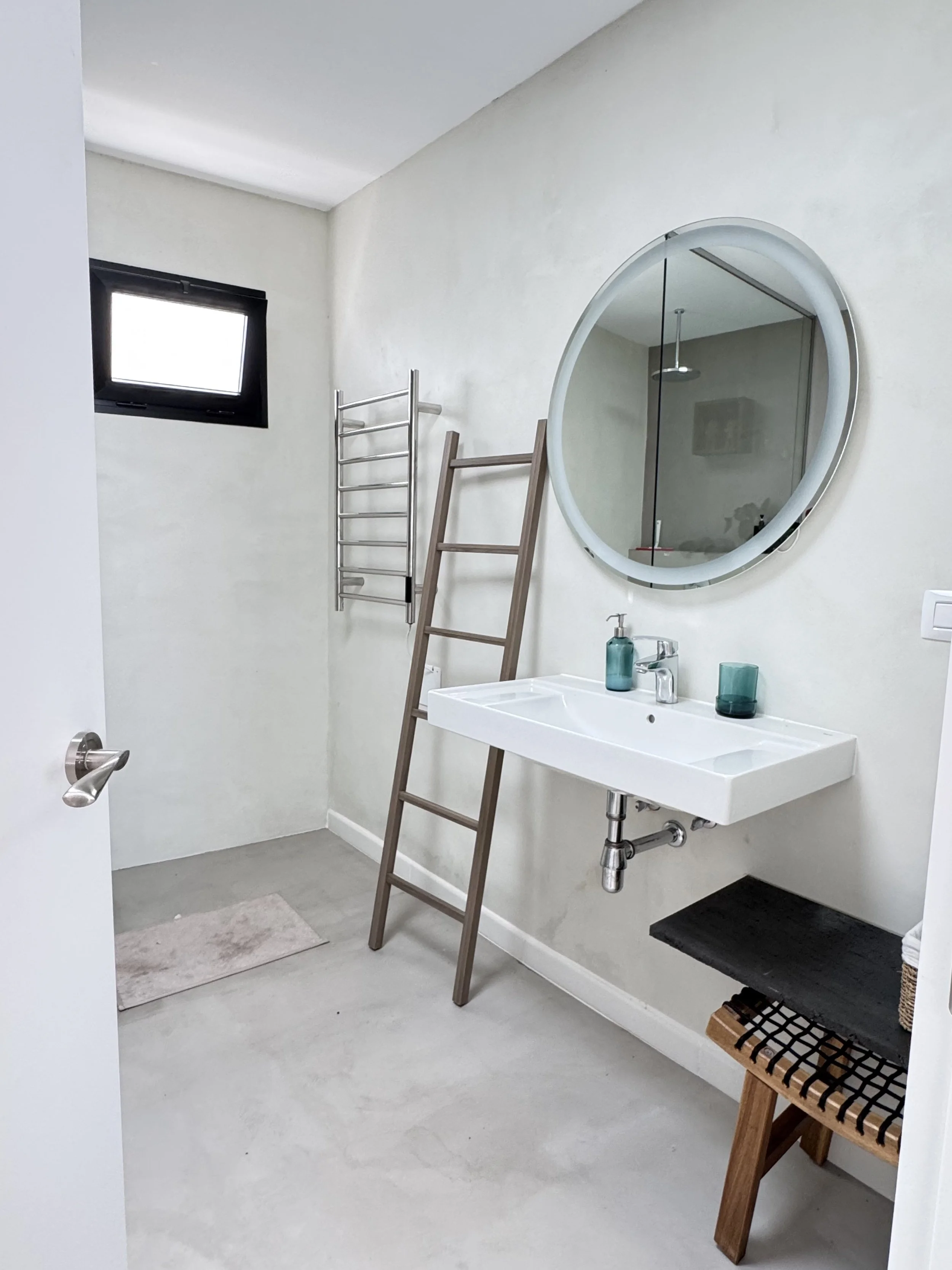 Minimalist bathroom with round mirror and wooden ladder at Casita Luna Lanzarote