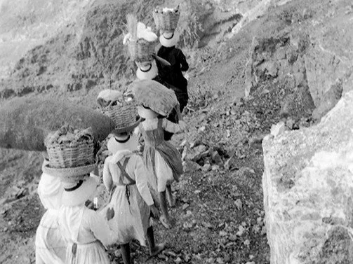 Women carrying heavy baskets while climbing the rocky Camino de los Gracioseros.