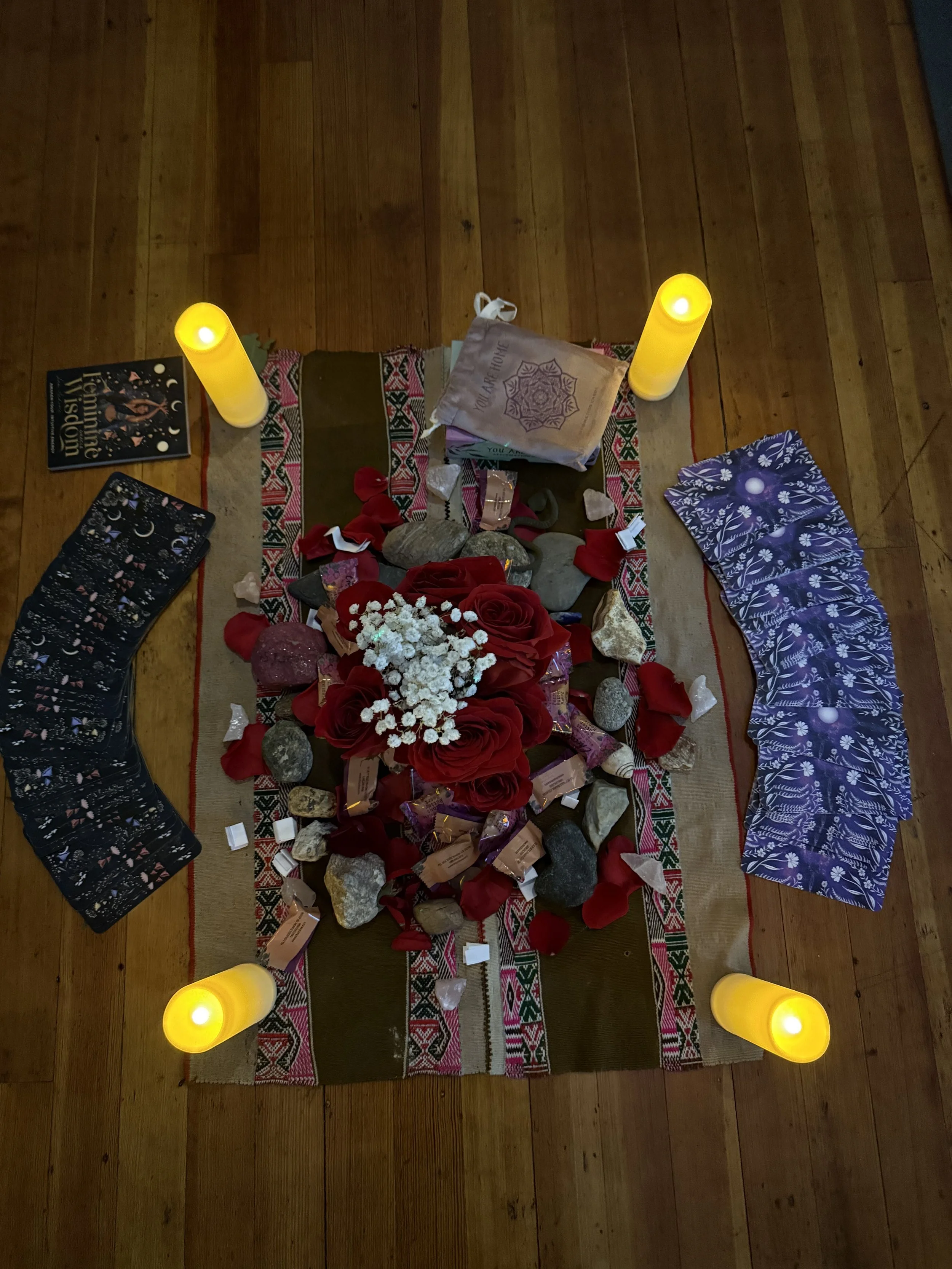 A spiritual or memorial altar with candles, rocks, flowers, and decorative cloth, arranged on a wooden floor.