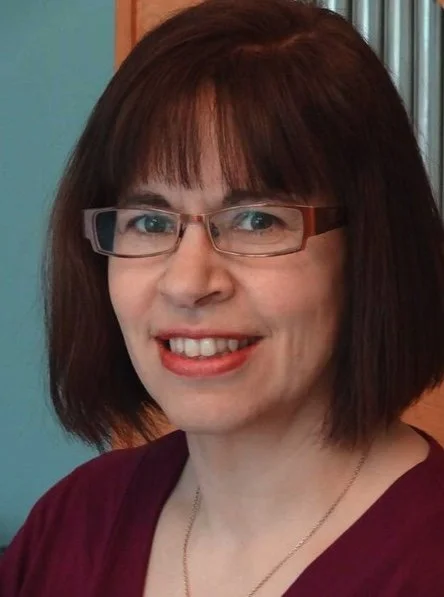 A woman with shoulder-length brown hair and glasses smiling at the camera.