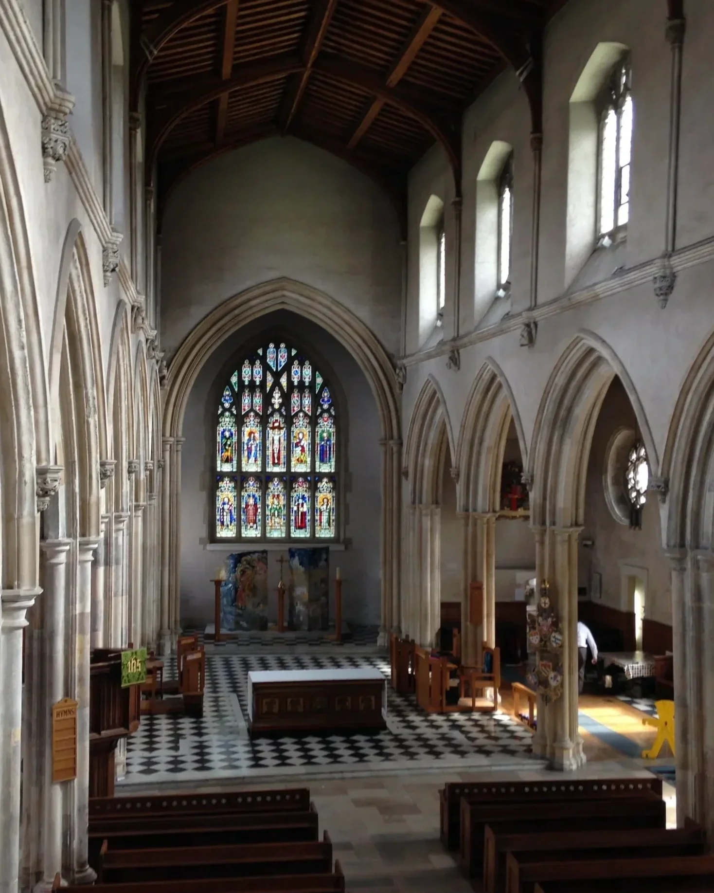 Interior of a church with high arched ceiling, stained glass window, and wooden pews.
