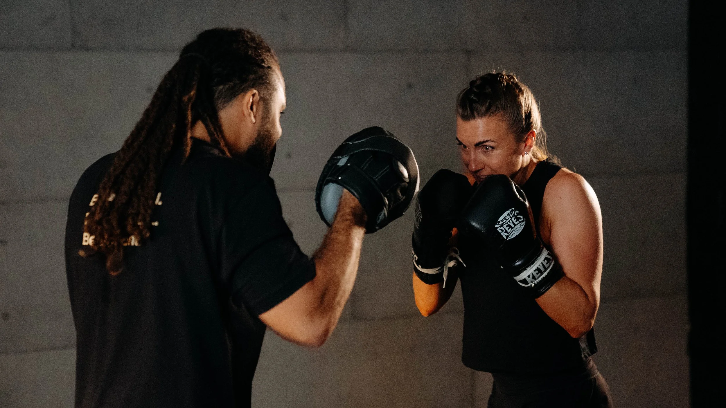 A woman and a man sparring with boxing gloves in a gym, facing each other with focus and determination.