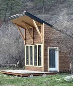 Small modern wooden house with large windows and a sloped roof, set outdoors.