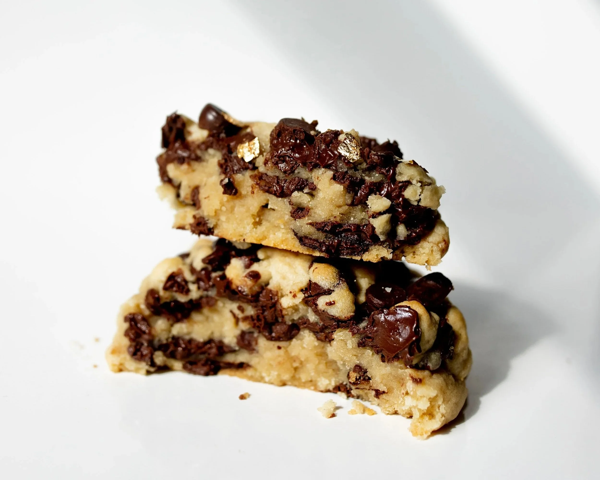 Two chocolate chip cookie bars stacked on a white surface with chocolate chunks and chips visible.
