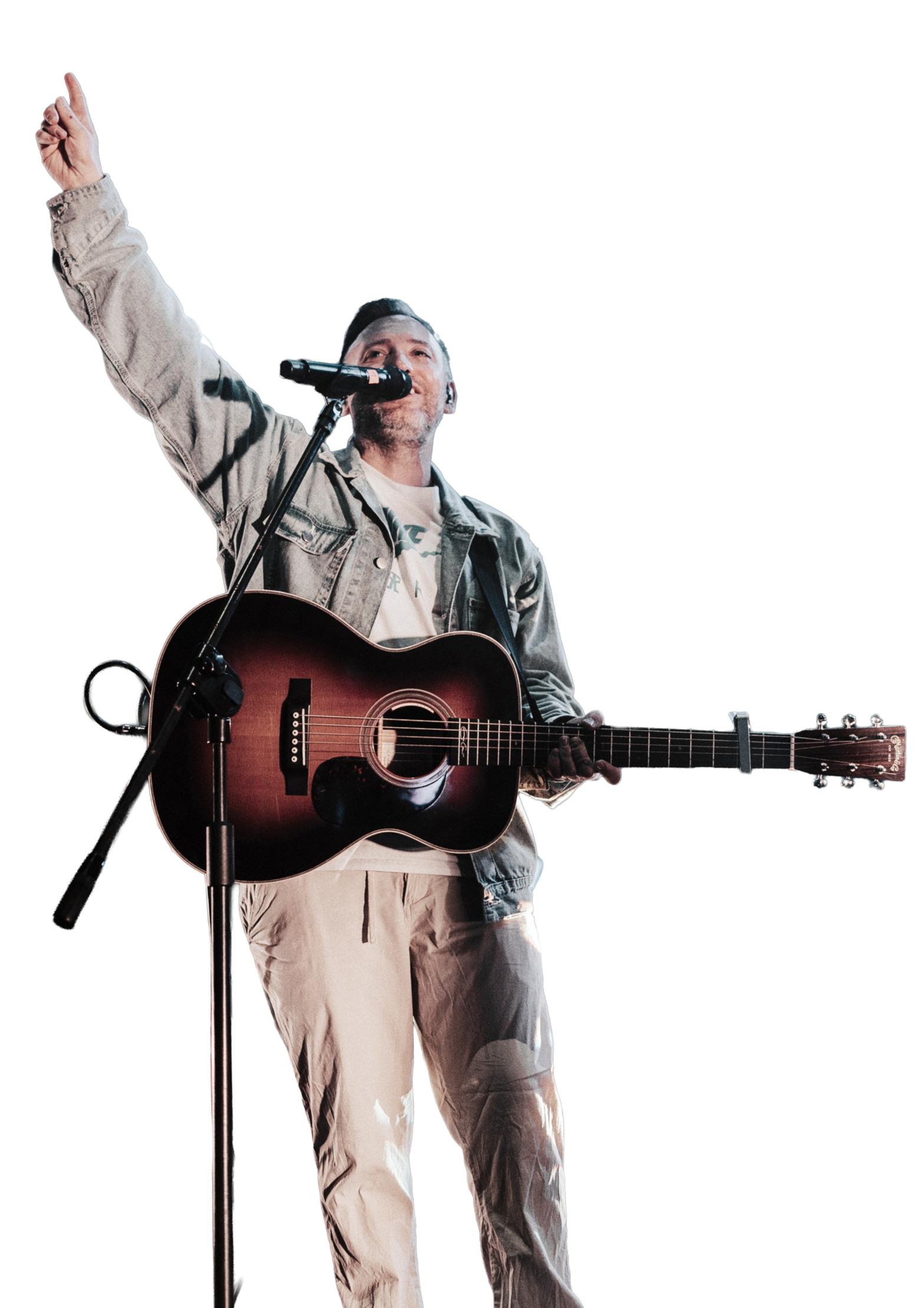 A man with a microphone, singing and playing an acoustic guitar on stage.