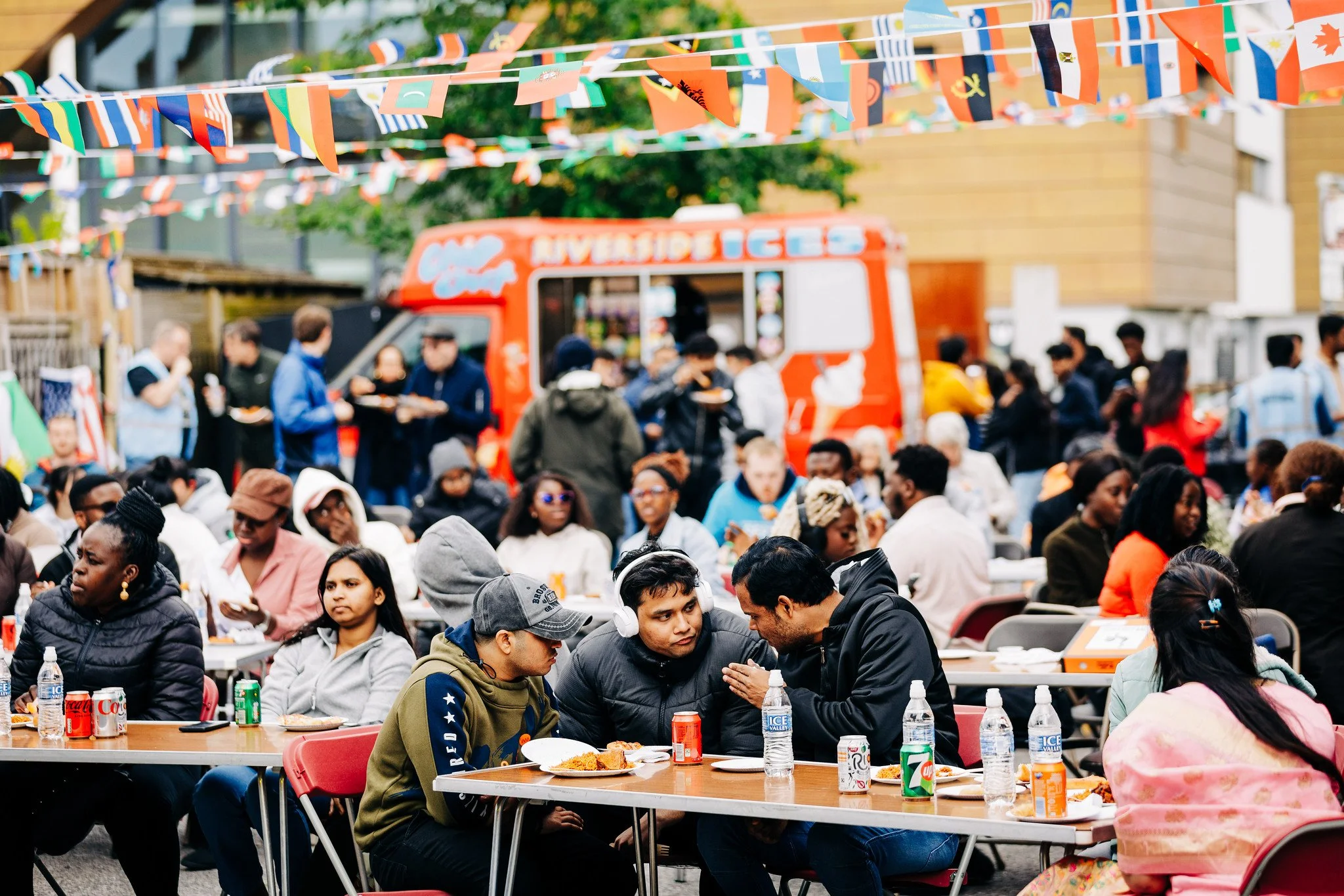 Crowd of people enjoying outdoor event with flags and food trucks.