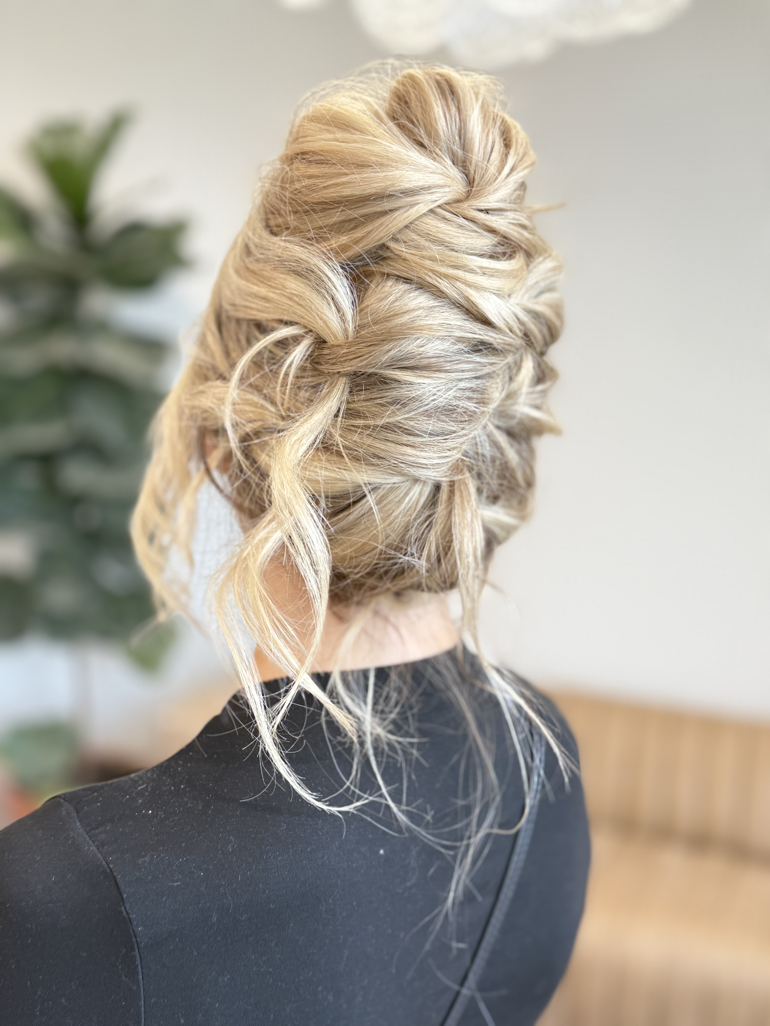 Back view of a woman with blonde, wavy hair styled in an elegant updo, wearing a black top.