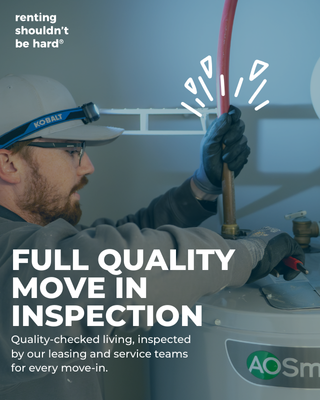 A technician inspecting a water heater with a red screwdriver, wearing safety glasses and gloves, with a safety helmet with a brand logo, in a professional service setting.