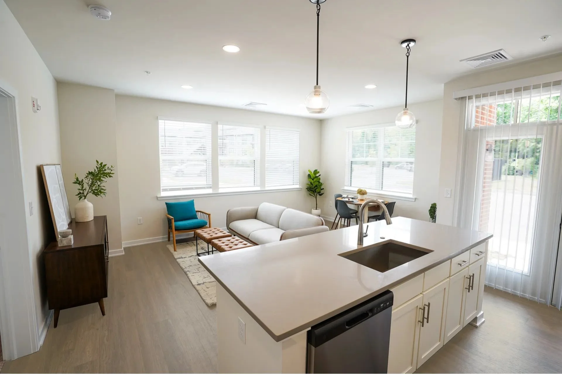Bright open living room and kitchen with white walls, large windows, modern furniture, and minimal decor.