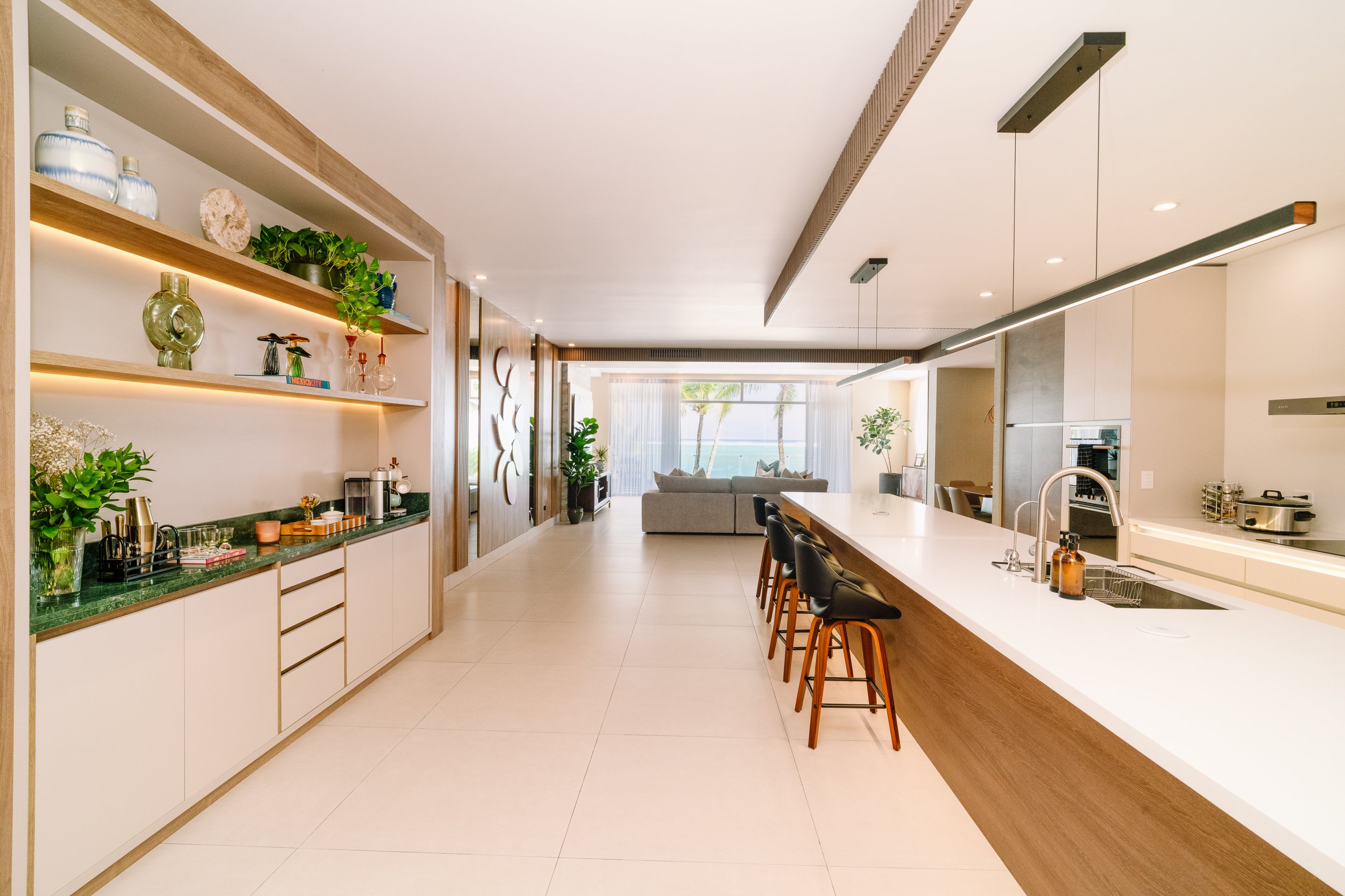 Modern open-concept kitchen and living room with bar seating, greenery, and ocean view.
