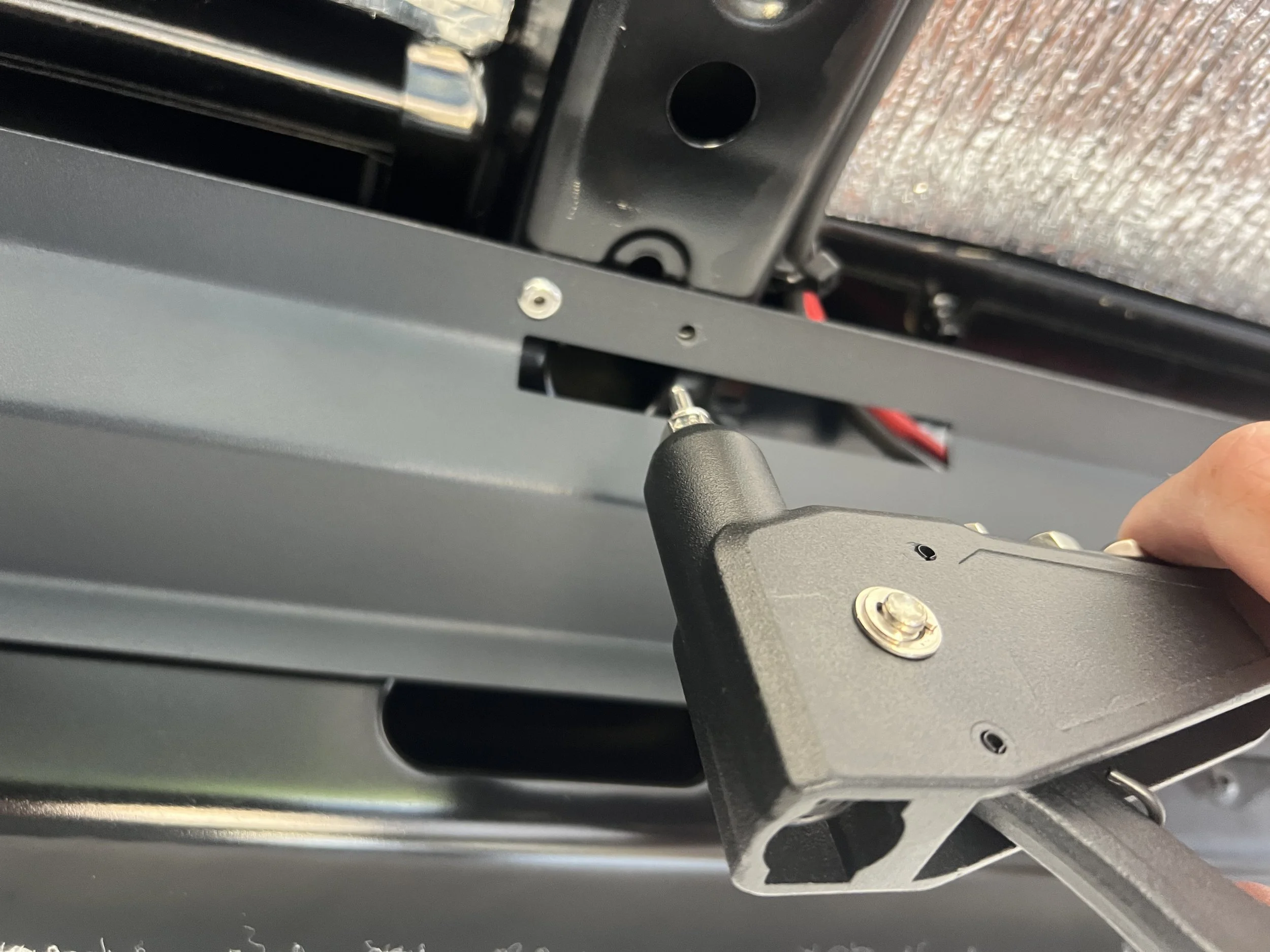 A person using a screwdriver to tighten a bolt on a metal bracket inside electronic or machinery equipment.