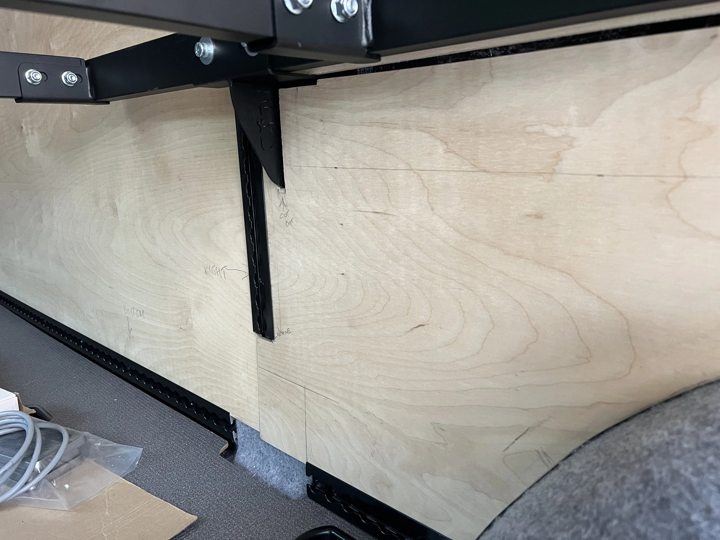 Part of a black metal adjustable stand or shelf attached to a wooden surface with handwritten labels and measurements.