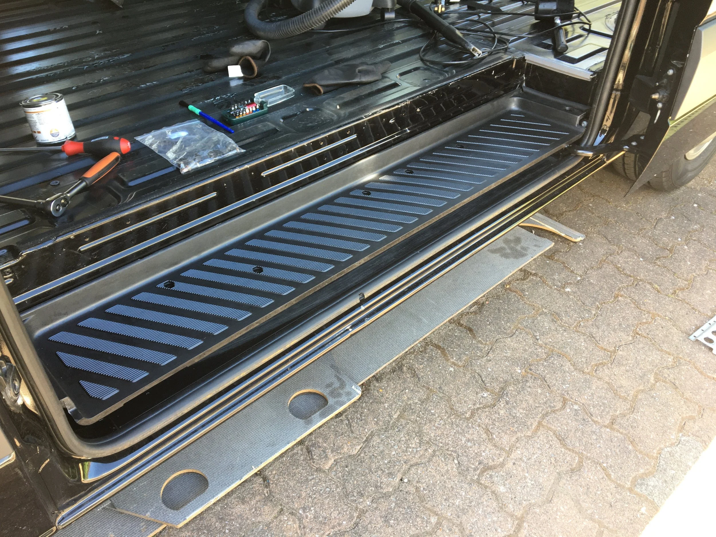 View of a vehicle's side step with tools and components, including screwdrivers and small hardware, on the vehicle's open side panel.
