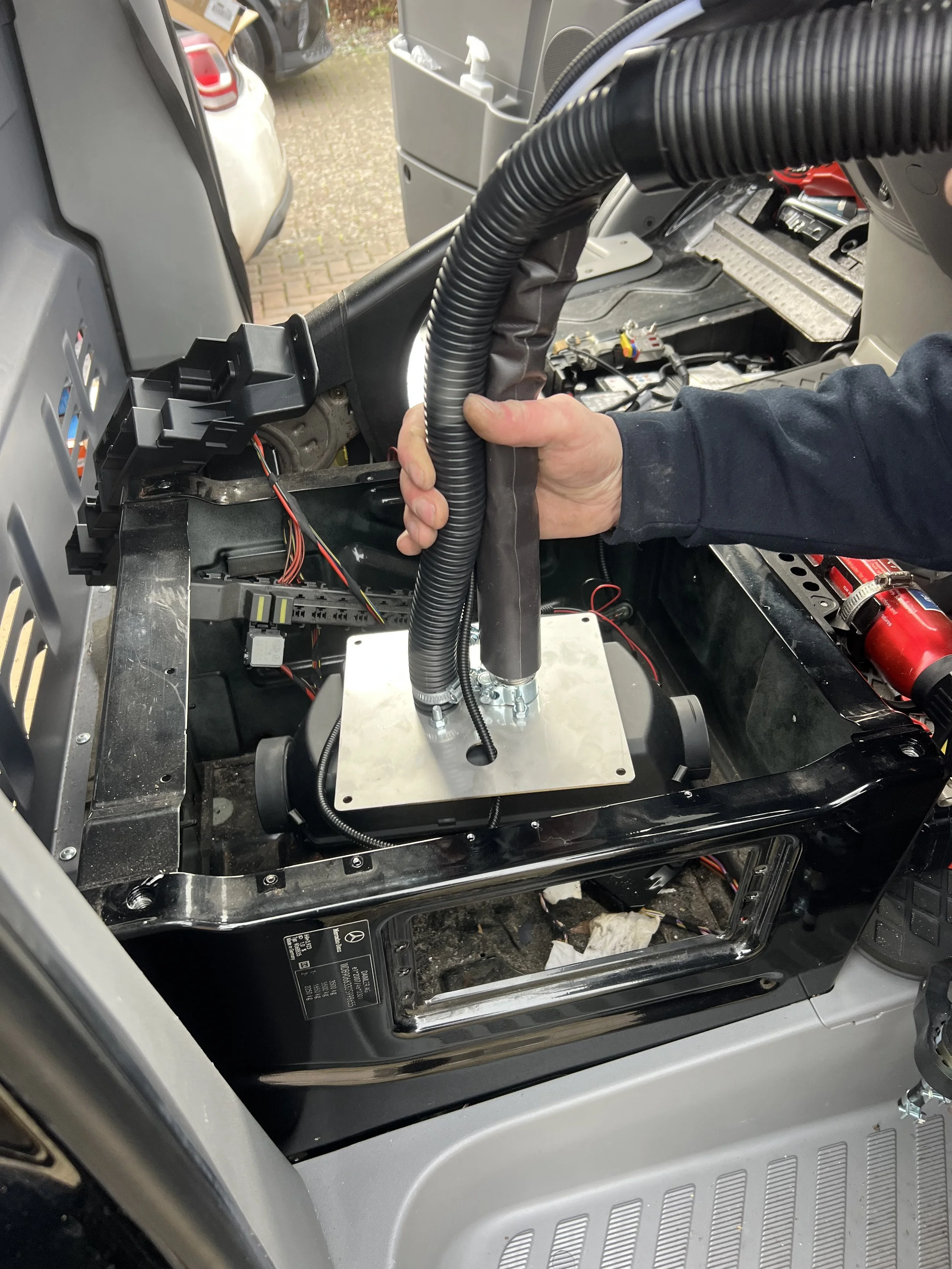 A person installing or repairing machinery inside a vehicle, with various tools and electronic components visible.