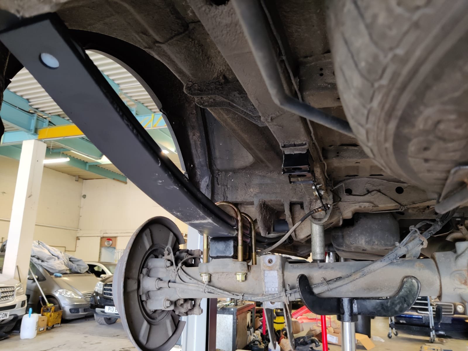 Underneath view of a vehicle's axle and suspension system being repaired in an automotive workshop.