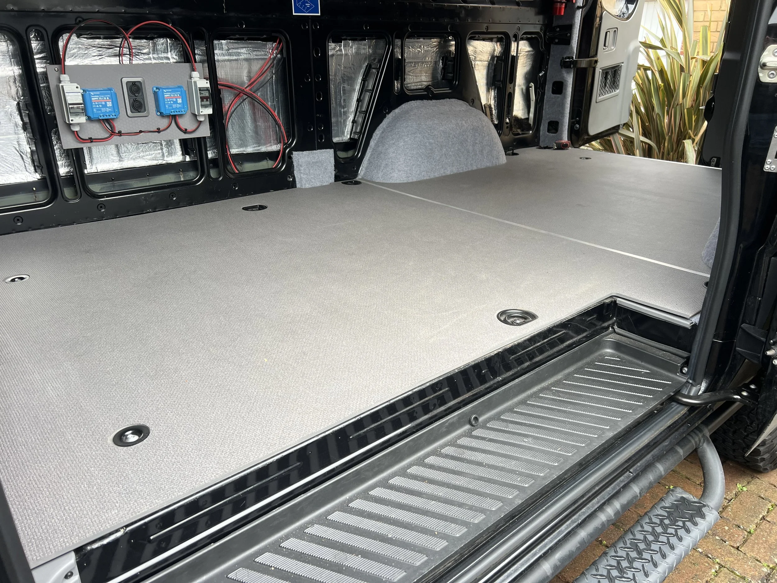 Interior of a vehicle with a flat load floor, showing wiring and electronic components on the back wall.