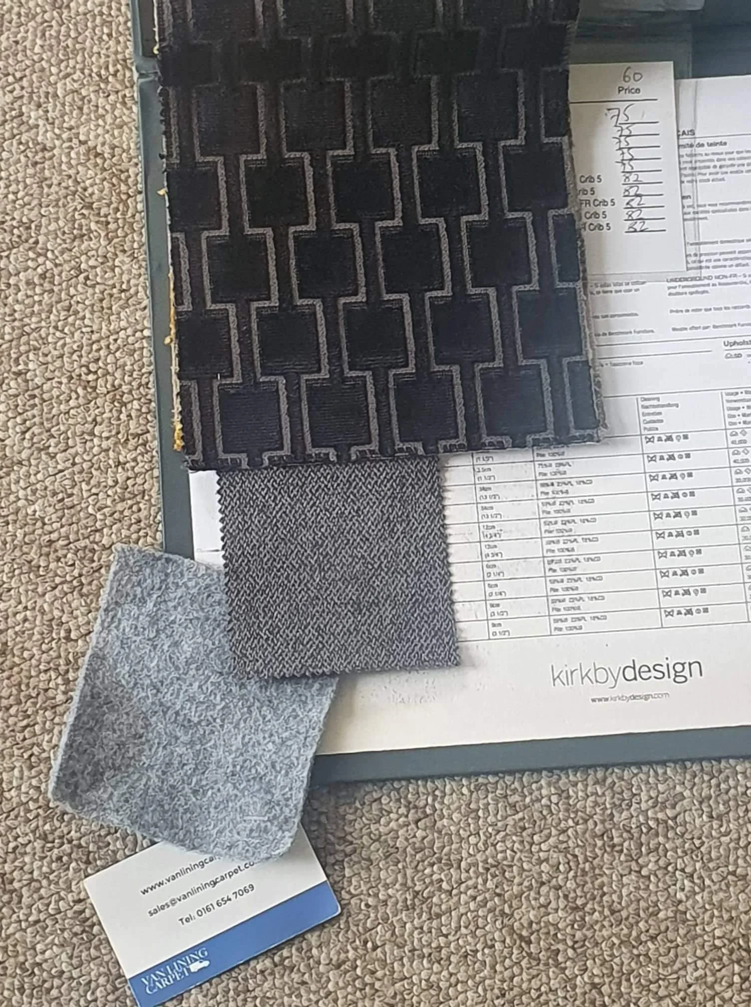 Three fabric samples in different shades of gray and black on top of a design sheet, with a business card and a handwritten price list to the side.