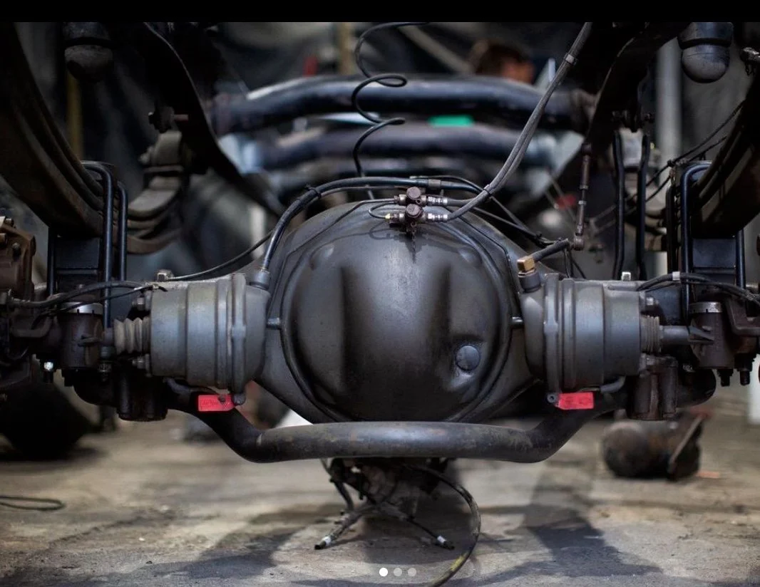 Close-up view of a car's differential with surrounding suspension components, wires, and hoses in a workshop or garage.