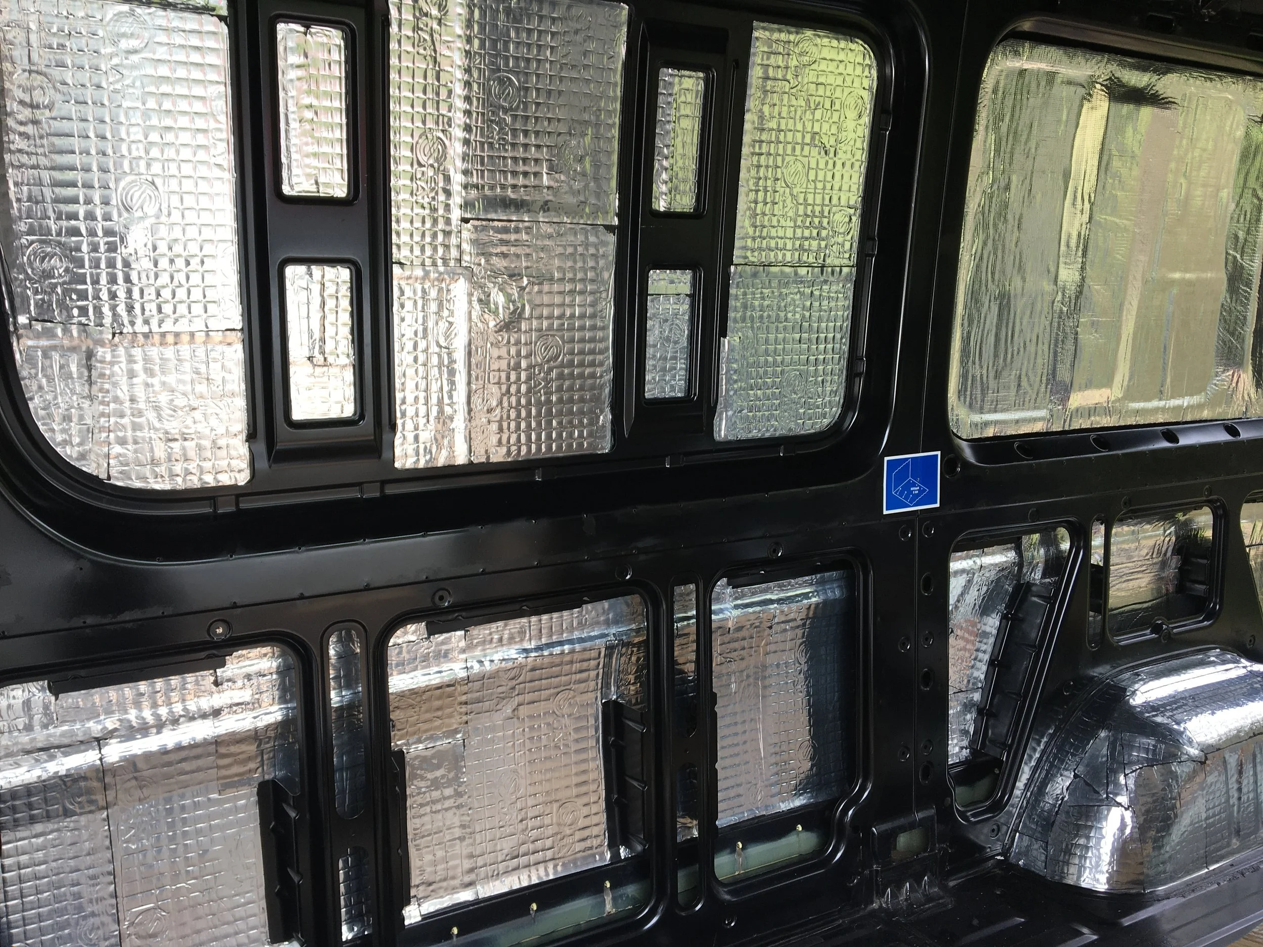 Interior of a vehicle frame with silver insulation panels and a small blue and white accessibility sign.