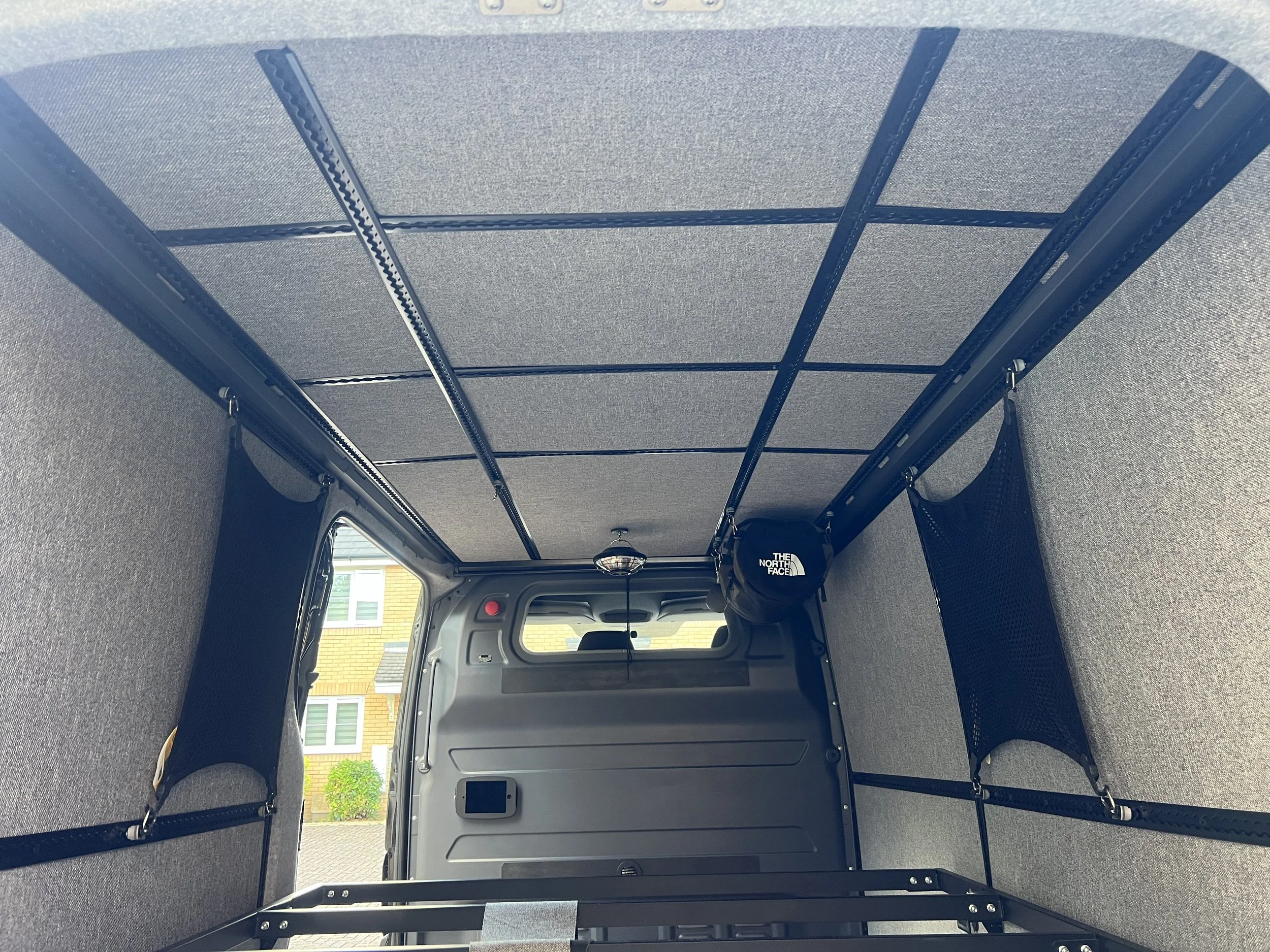 Inside a vehicle with a roof rack system installed, including metal rails, straps, and mesh storage pockets on the sides.
