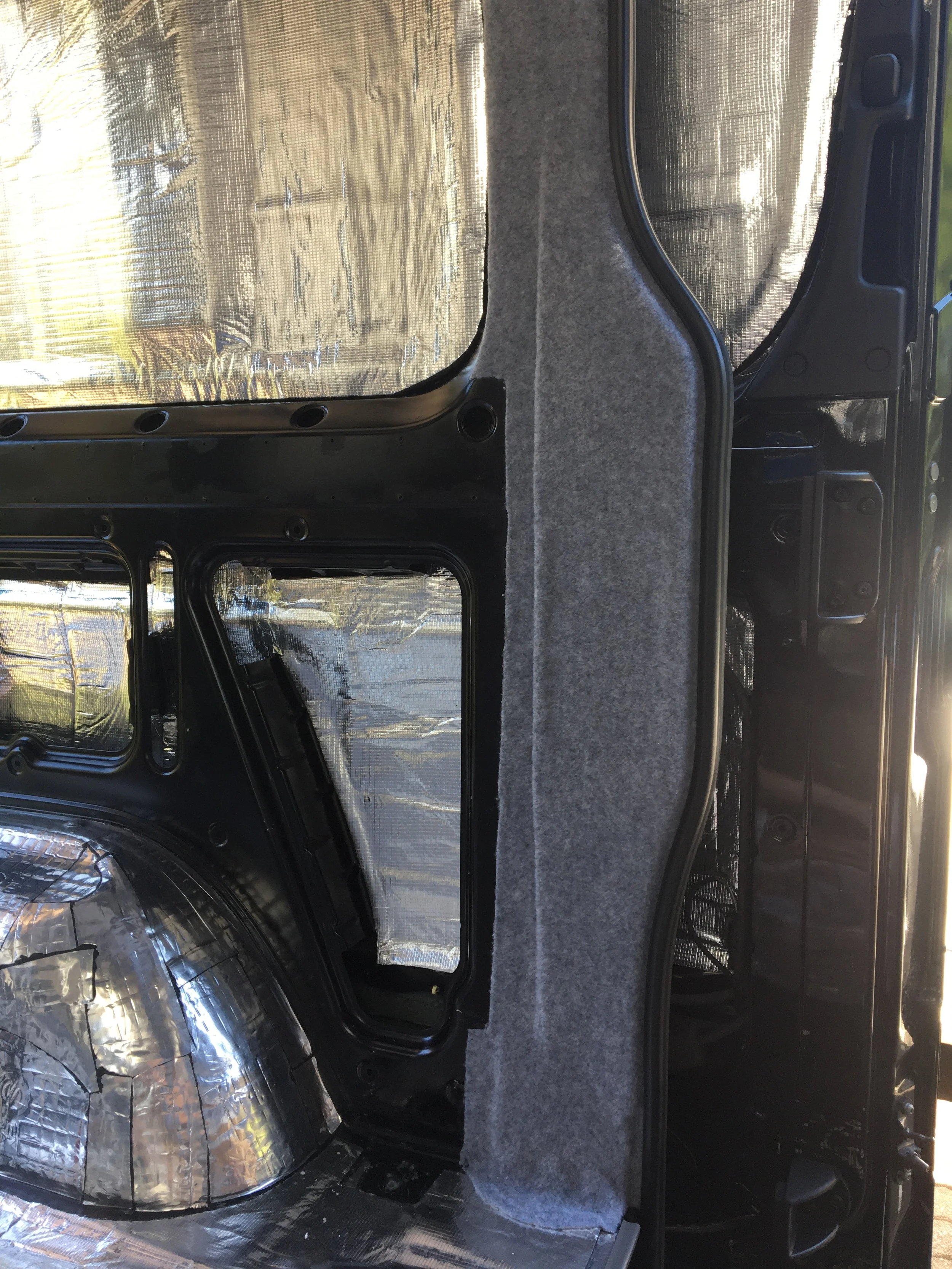 The interior of a vehicle with insulation and soundproofing materials, including a section of gray carpeted lining.