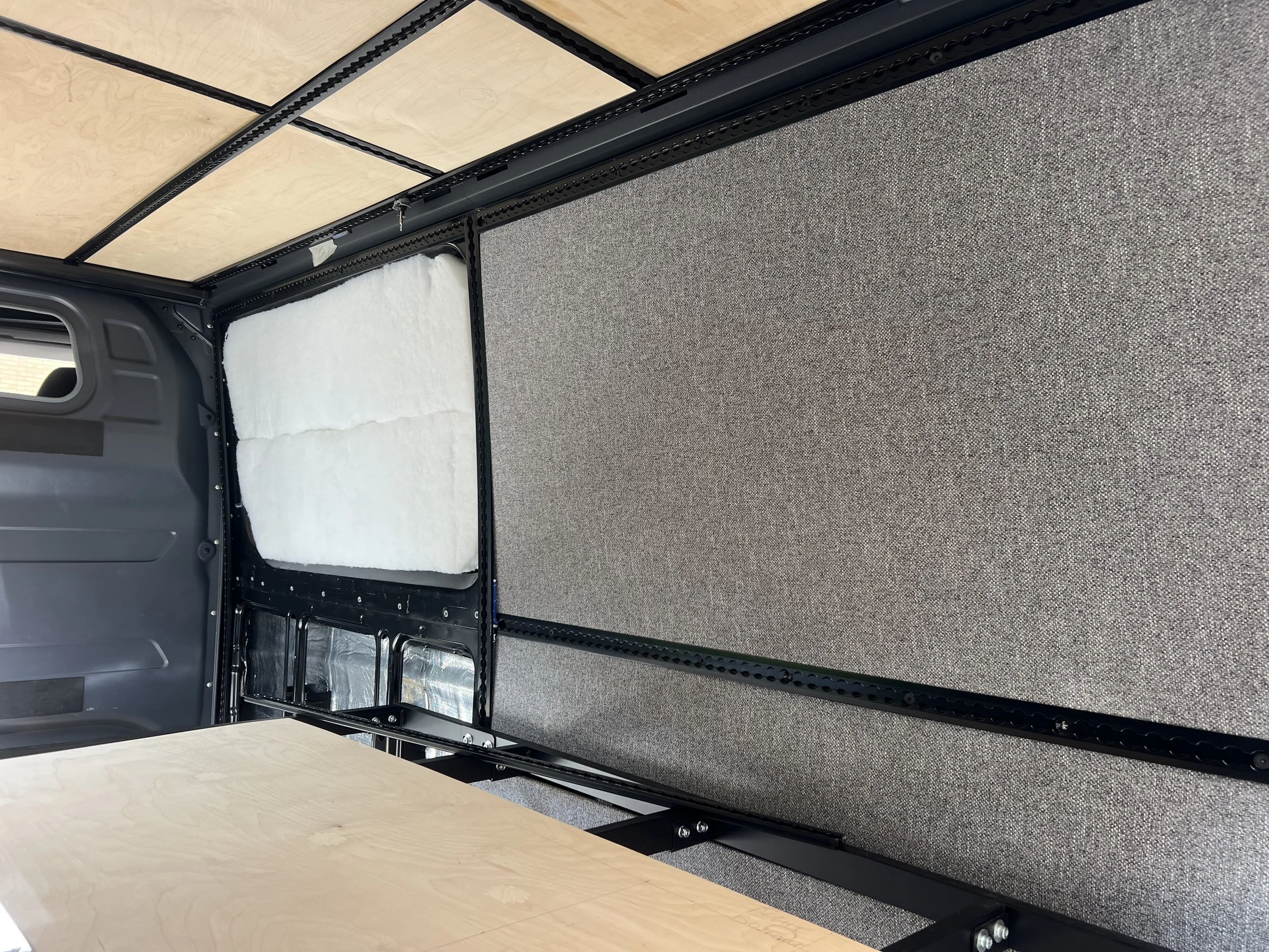 Interior of a vehicle modification with carpeted flooring, plywood ceiling panels, and black metal framing.