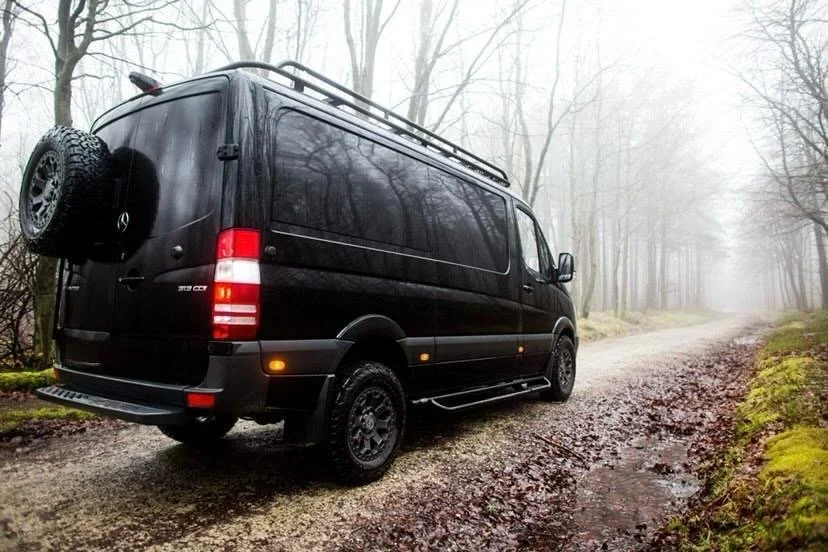 Black van parked on a dirt road in a foggy forest.