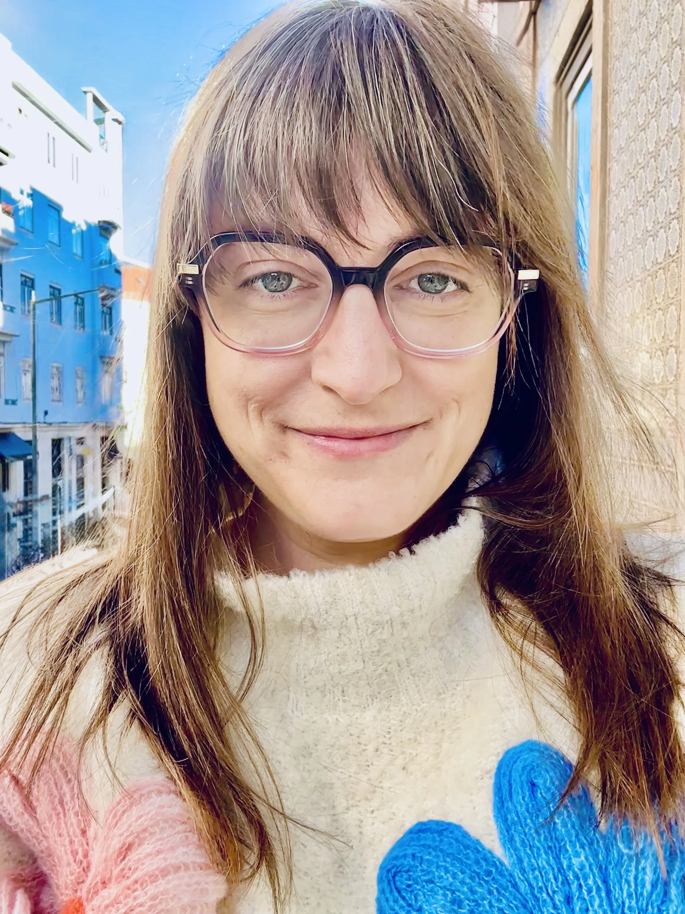 A portrait of Krisi Johnson, smiling outside, with buildings and a bright sky in the background.