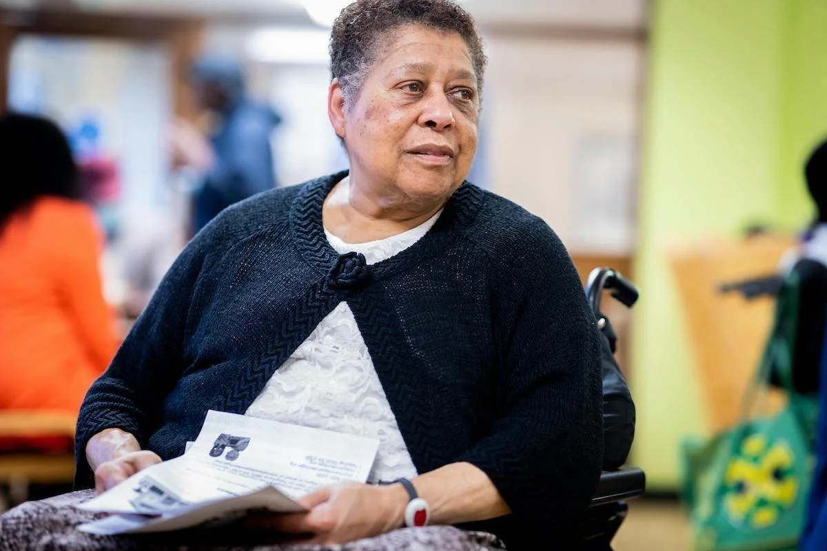 Elderly woman seated in a wheelchair receiving assistance at home