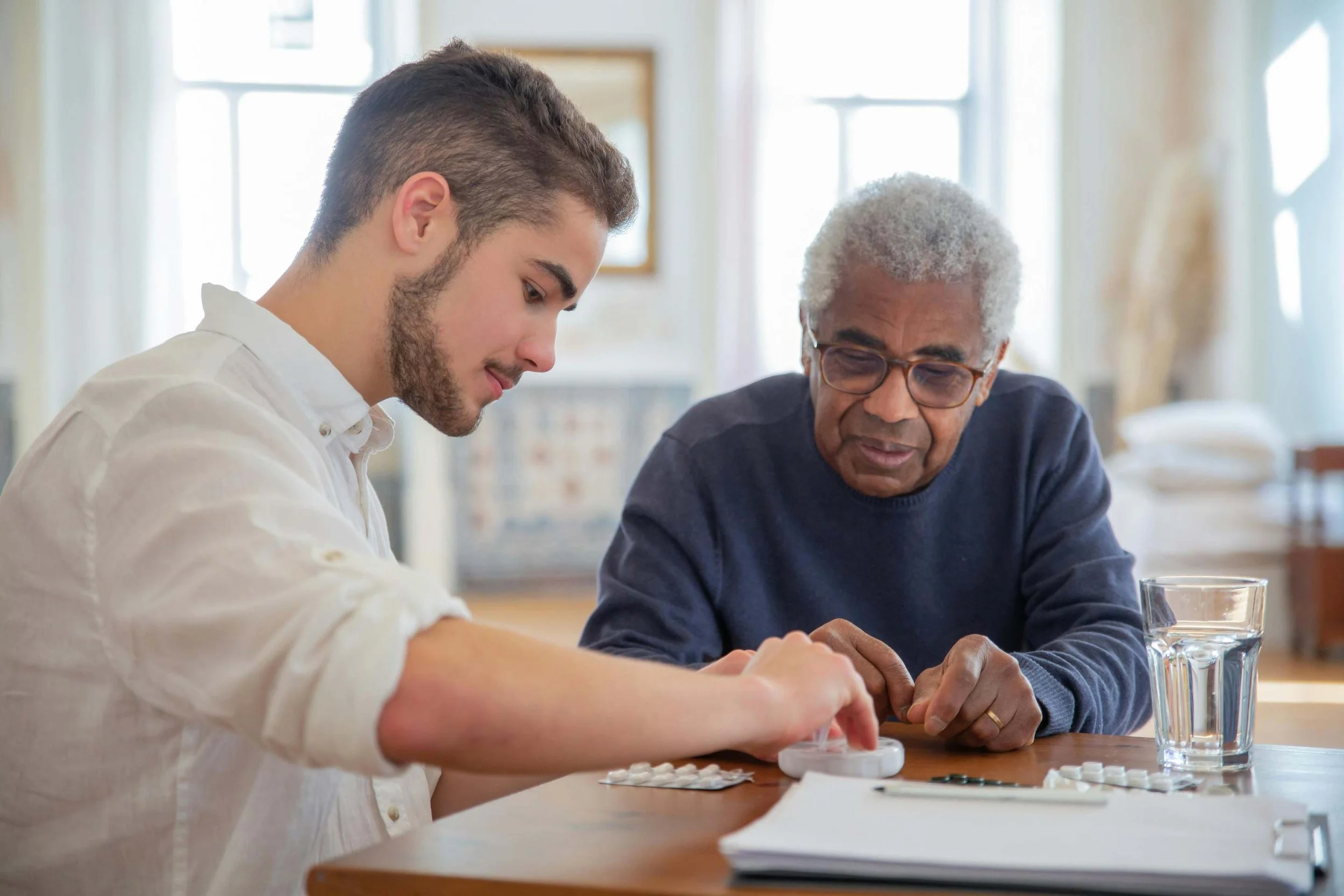 Caregiver assisting an elderly man with medication reminders during a home care visit