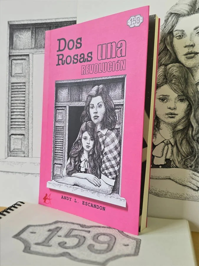 Photo of the published novel “Dos Rosas, una revolución” placed alongside the original ink drawings used for its cover design, including a portrait of mother and daughter, a Cuban window frame, and a house number plaque.