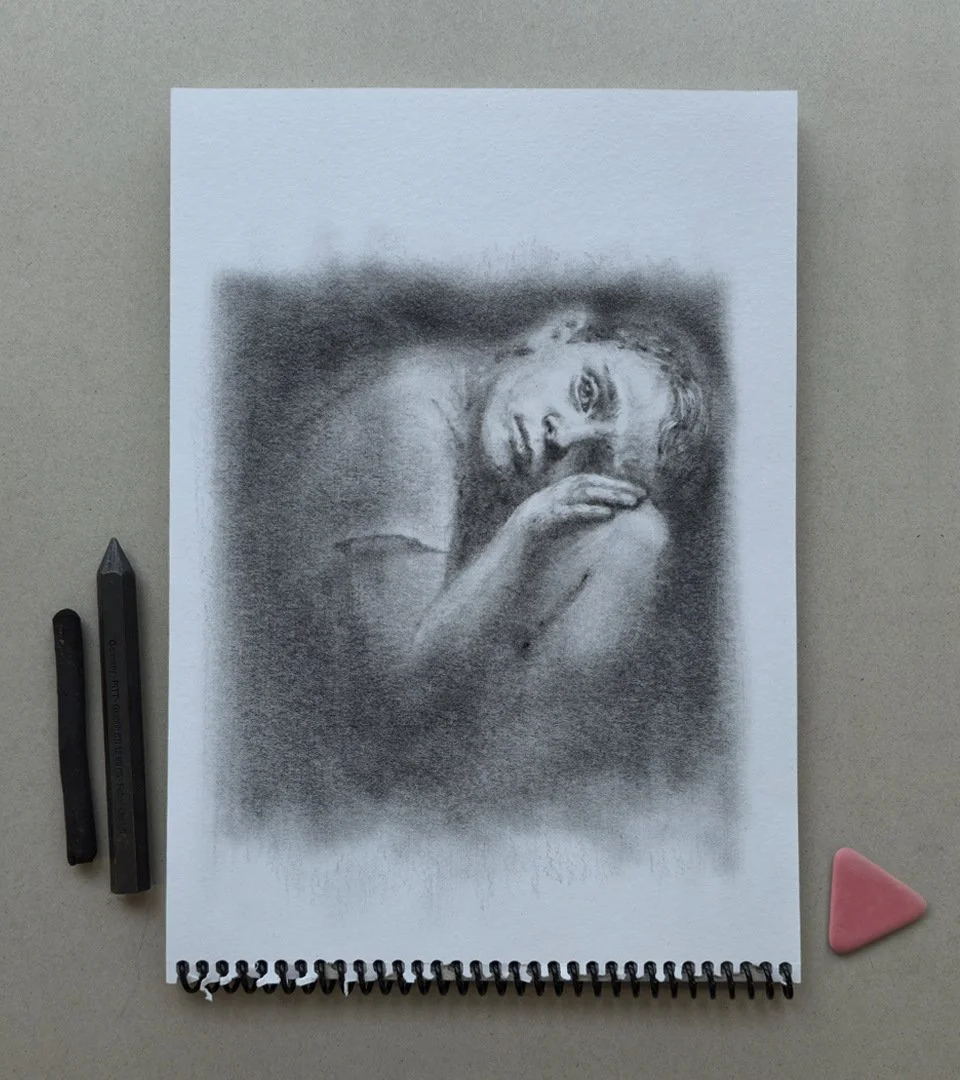 Charcoal drawing “EL DESPERTAR DE GULLIVER” by Daniel Perez Cabrera: child illuminated by eraser strokes on graphite, symbolizing self-discovery and healing, photographed in original format on work table.
