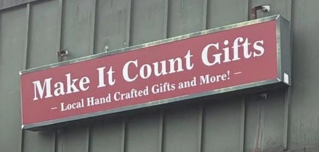 Sign for 'Make It Count Gifts,' a store selling locally handcrafted gifts, mounted on a gray wall.