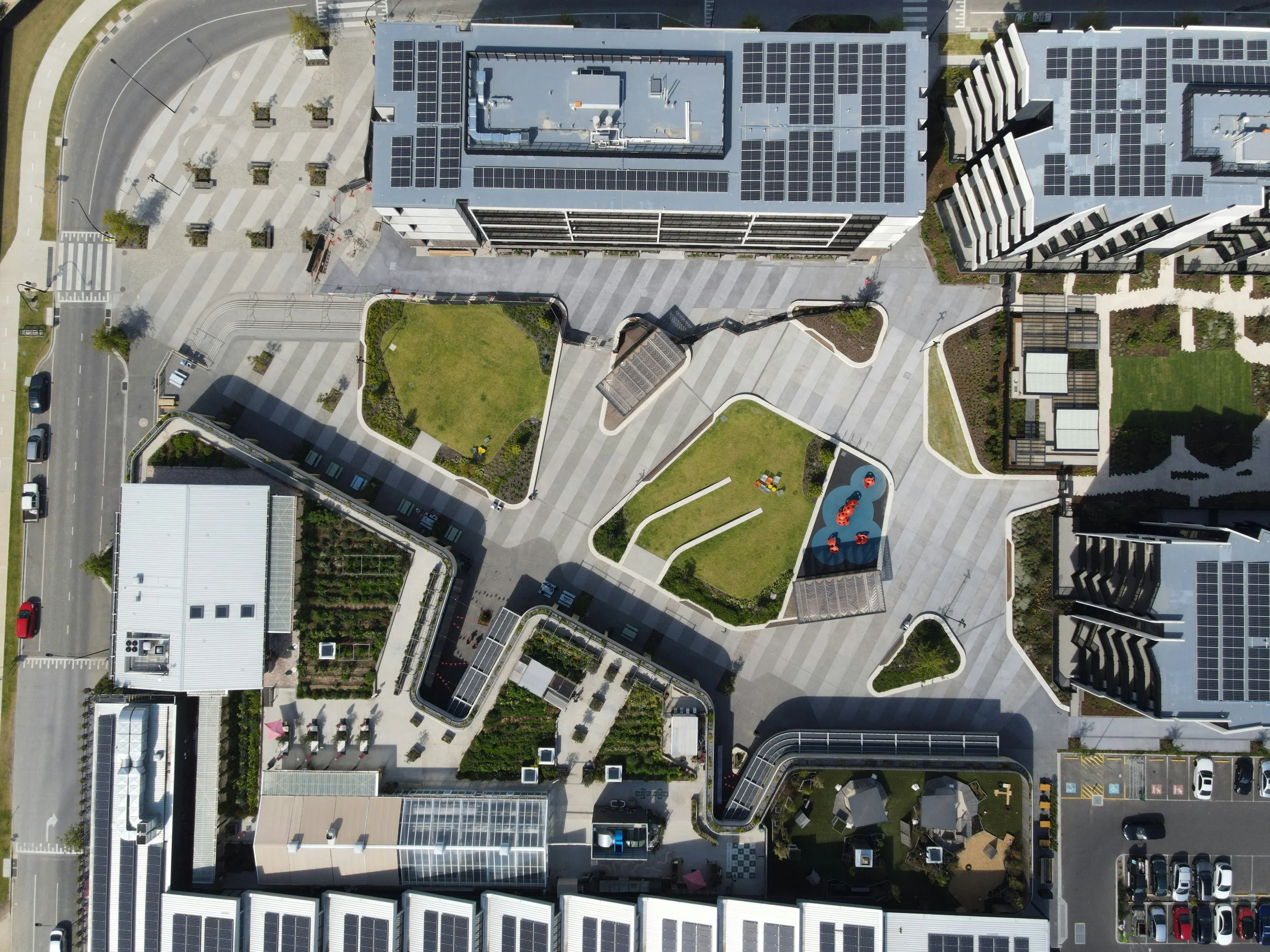 Aerial view of a modern urban rooftop with green spaces, pathways, and solar panels on surrounding buildings.